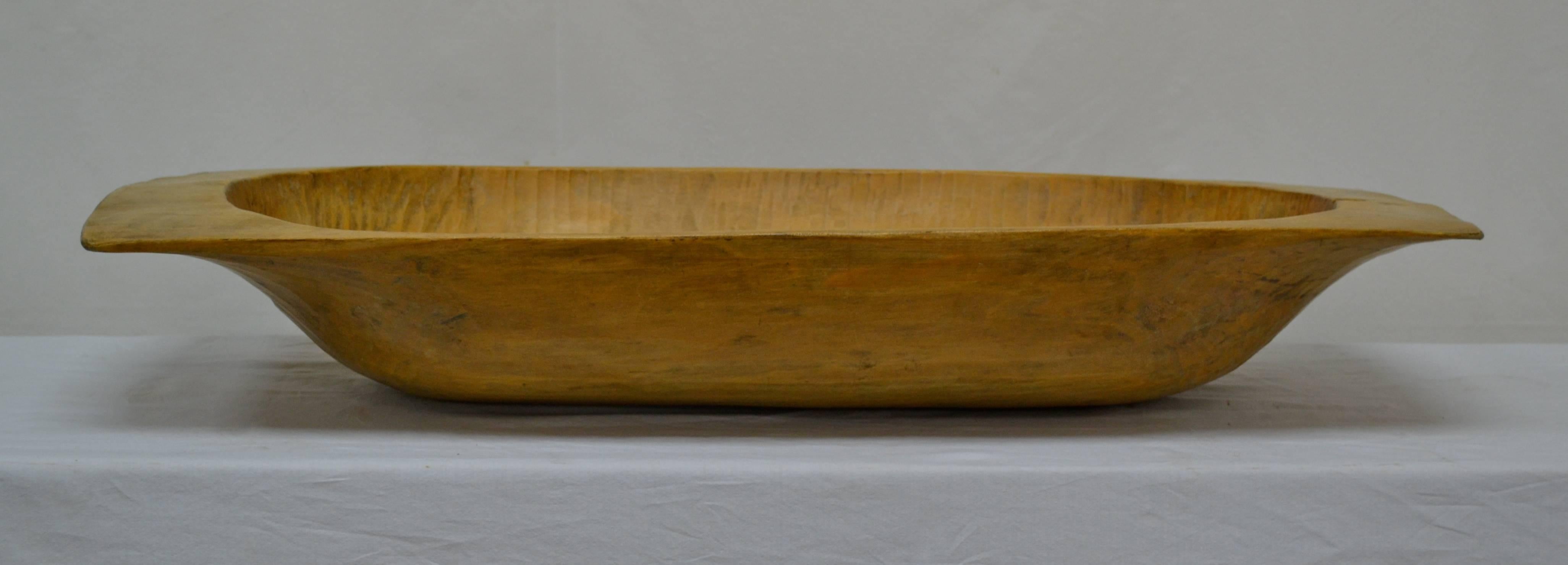 An antique wooden dough bowl or trog, hand-carved from a split log.  This one is a very versatile small size with one or two superficial cracks and a warm honey colour.  Great as a centerpiece or as a hallway catch-all.  Use for logs or magazines by
