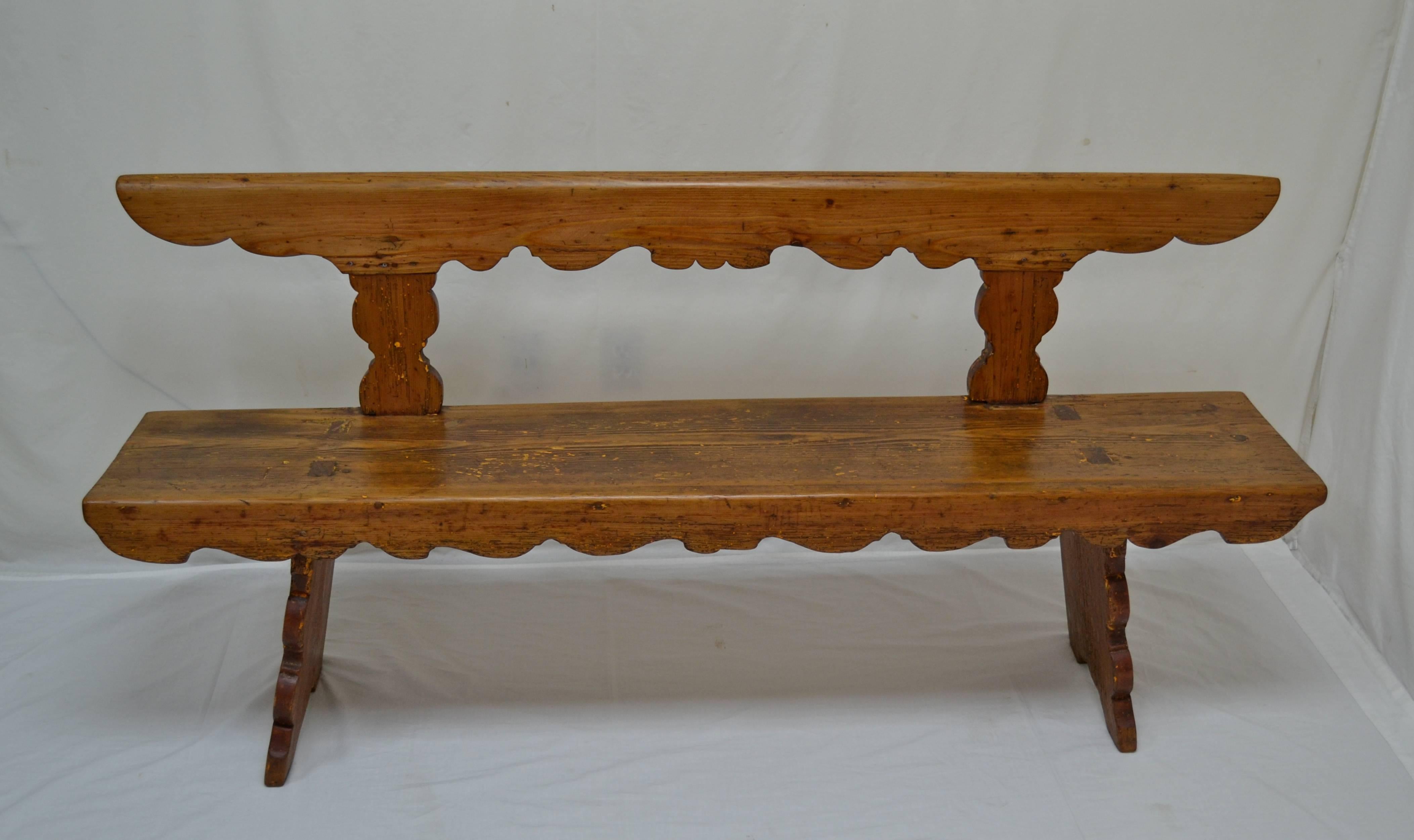 This is a beautiful rustic pine bench or settle in traditional Hungarian style. The sturdy back rail is straight on the top, rounded and worn smooth, and scalloped on the underside, a theme repeated on the front rail. Two shapely splats attach the