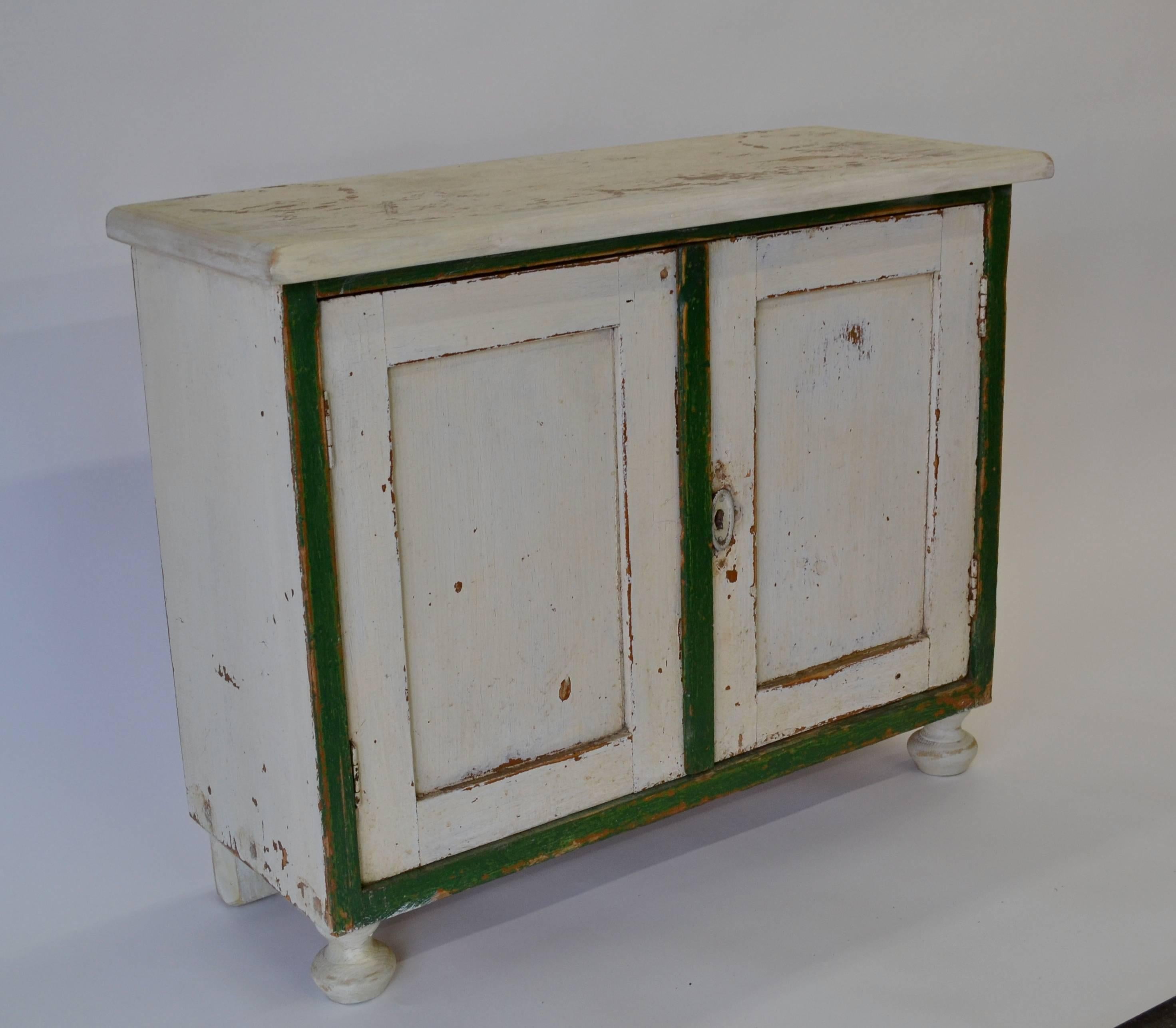 A lovely little two-door pine water cupboard on turned feet with very attractive wear to the finish. In old worn white paint with dark green trim, Hungary, circa 1910.