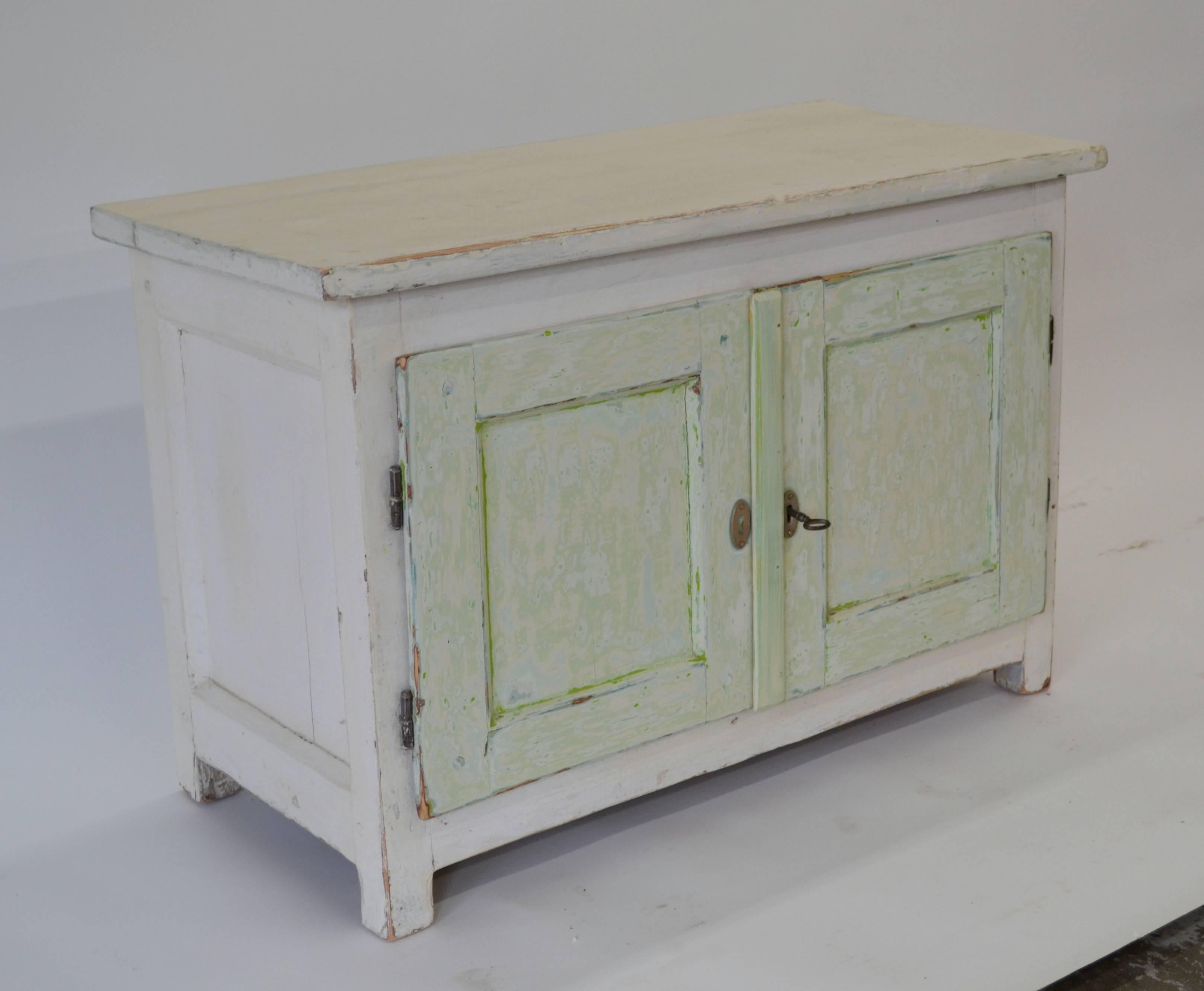 A useful little pine water cupboard with wide-swinging doors, paneled sides, and an attractive planked interior. In old worn green and white paint.