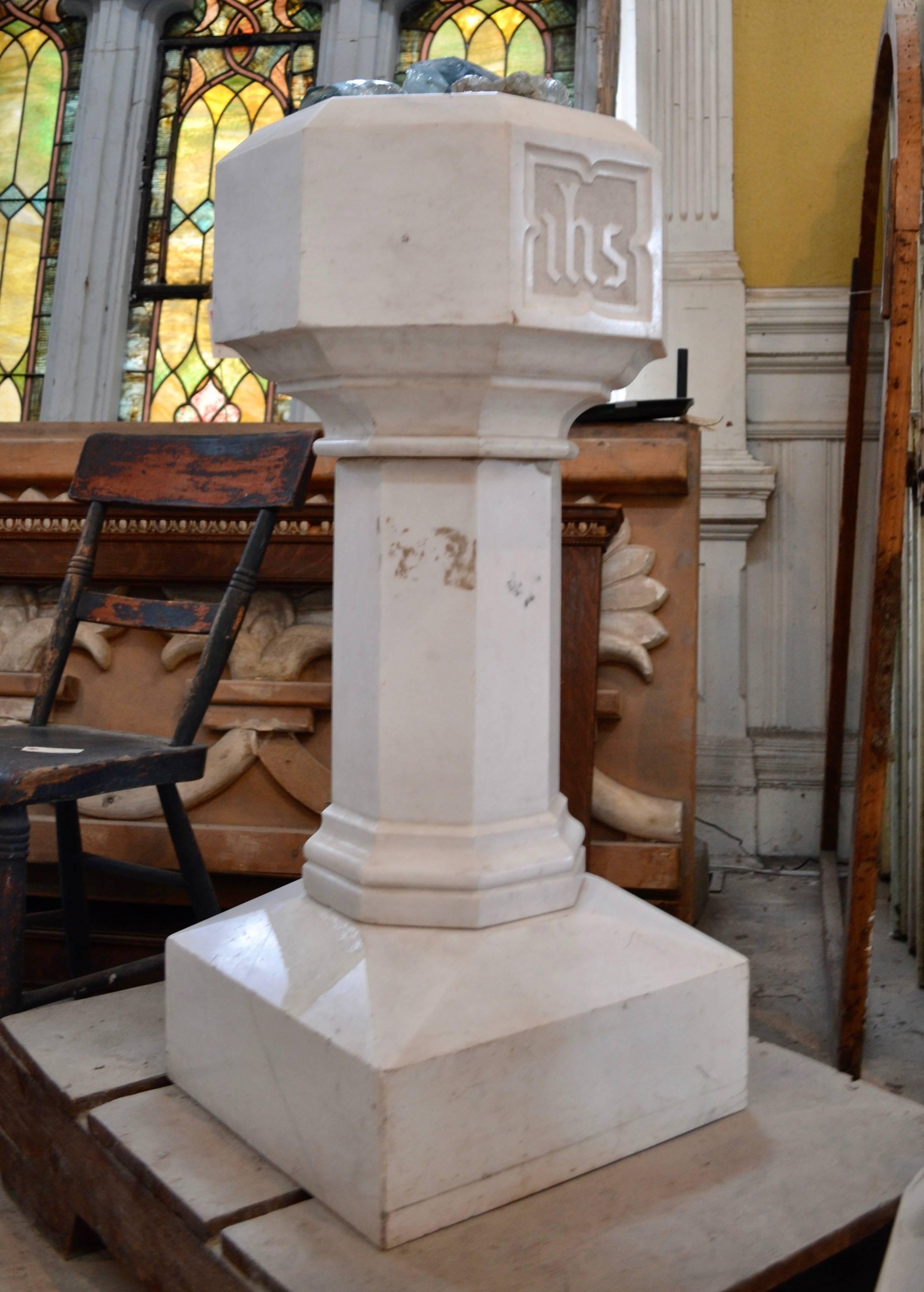 A hexagonal baptismal font on a square base from Baltimore City Church. The front panel bears the initials ihs (Iesus Hominum Salvator or In Hoc Signo) in bas-relief. Made from Carrara statuary marble. This piece is suitable for indoor or outdoor