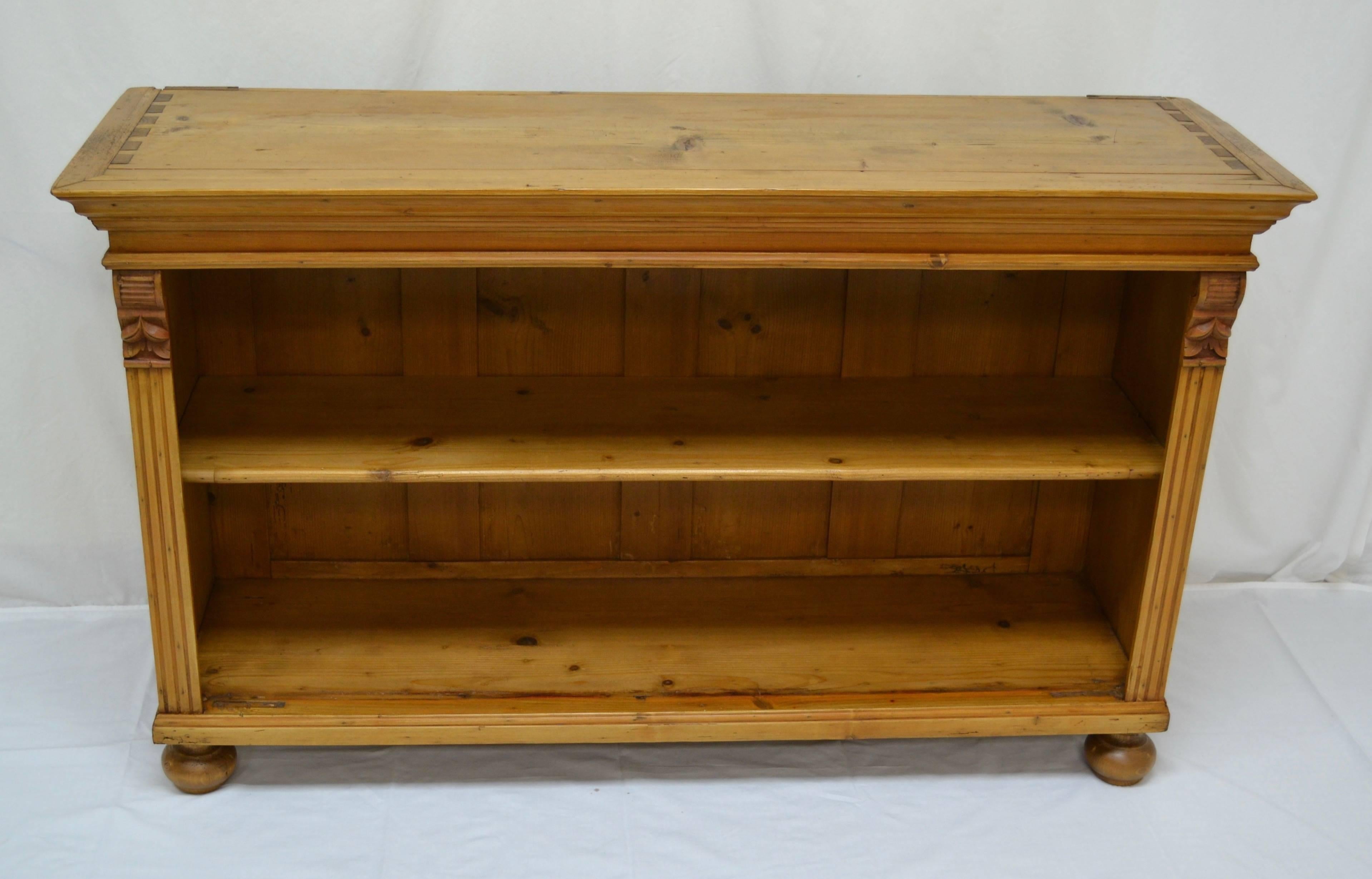 This unusually low pine open bookcase was once the upper section of a two piece buffet that lost its base.  With the addition of antique turned feet it makes this wonderful little bookcase.  Beneath a flat top with exposed dovetails and a bold crown
