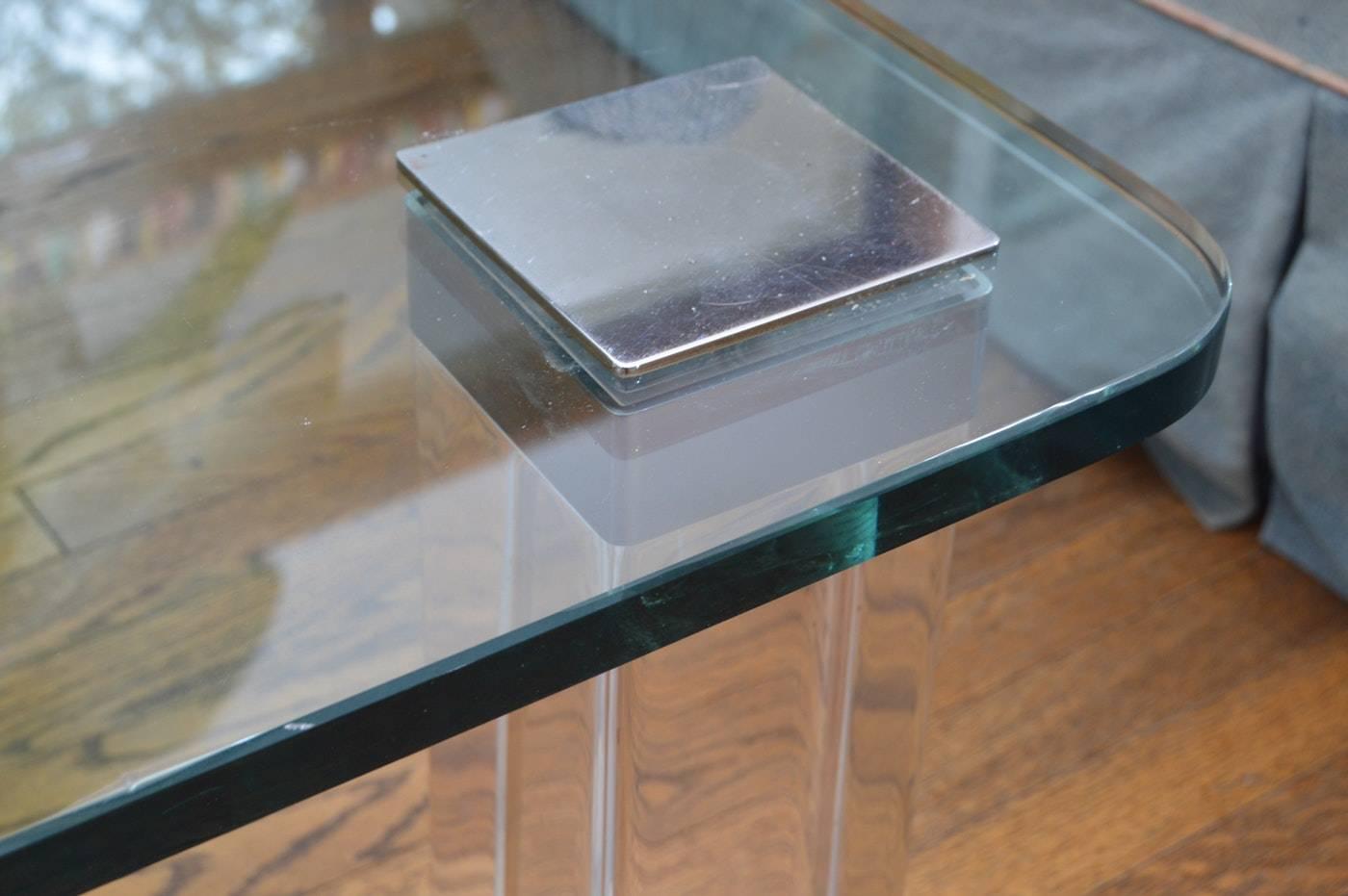 Belle table basse conçue et fabriquée dans les années 1970 et exécutée en Lucite et nickel poli avec un beau plateau en verre.
La table a des pieds carrés de 3 pouces en Lucite, coiffés d'inserts en nickel poli qui maintiennent le verre et les