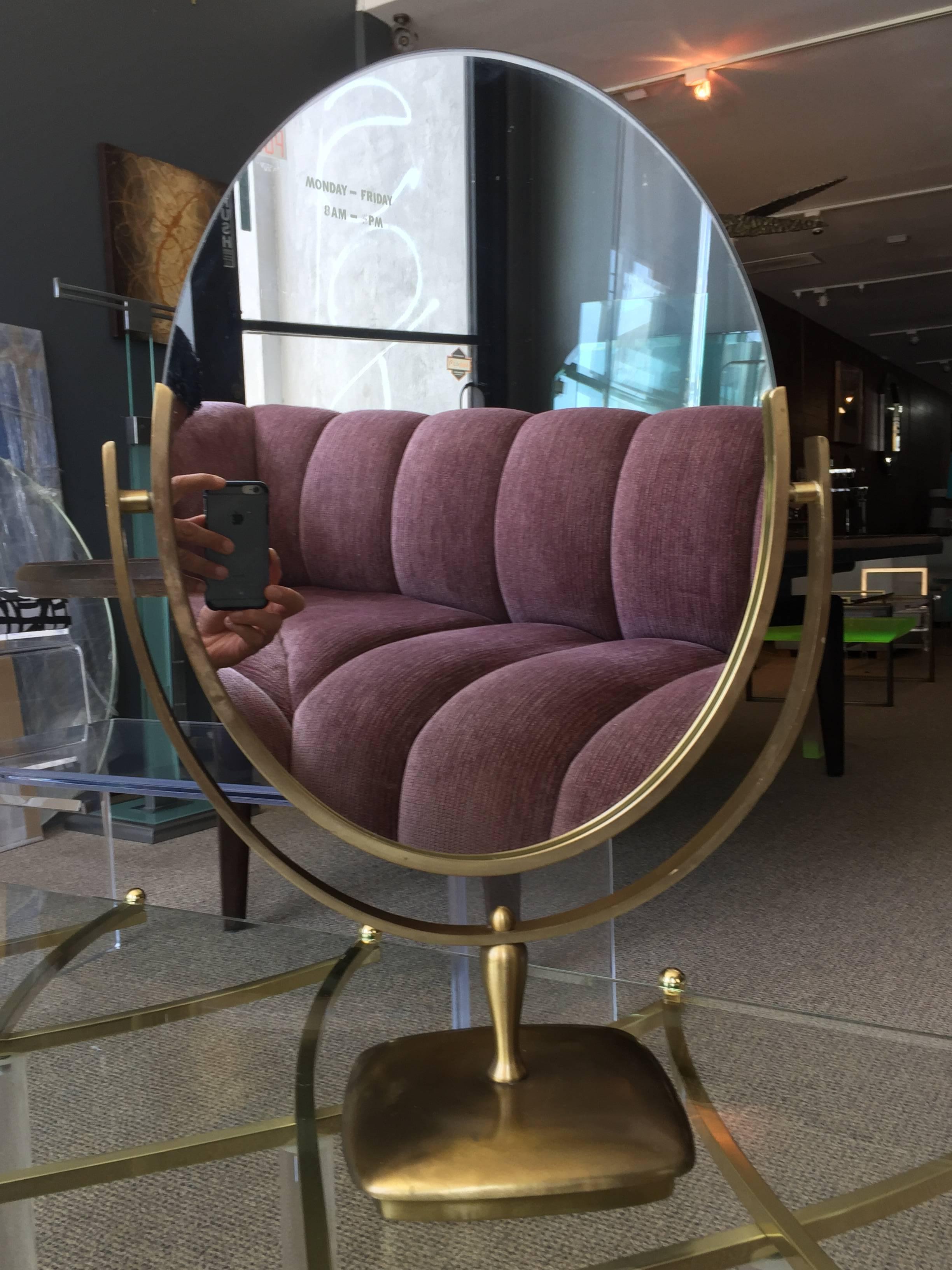 Large and beautiful oval mirror designed and manufactured by Charles Hollis Jones in the 1960s.
The mirror has an antique brass finished frame and base, the mirror is double sided and it can be flipped to be used on either side.

Measurements: