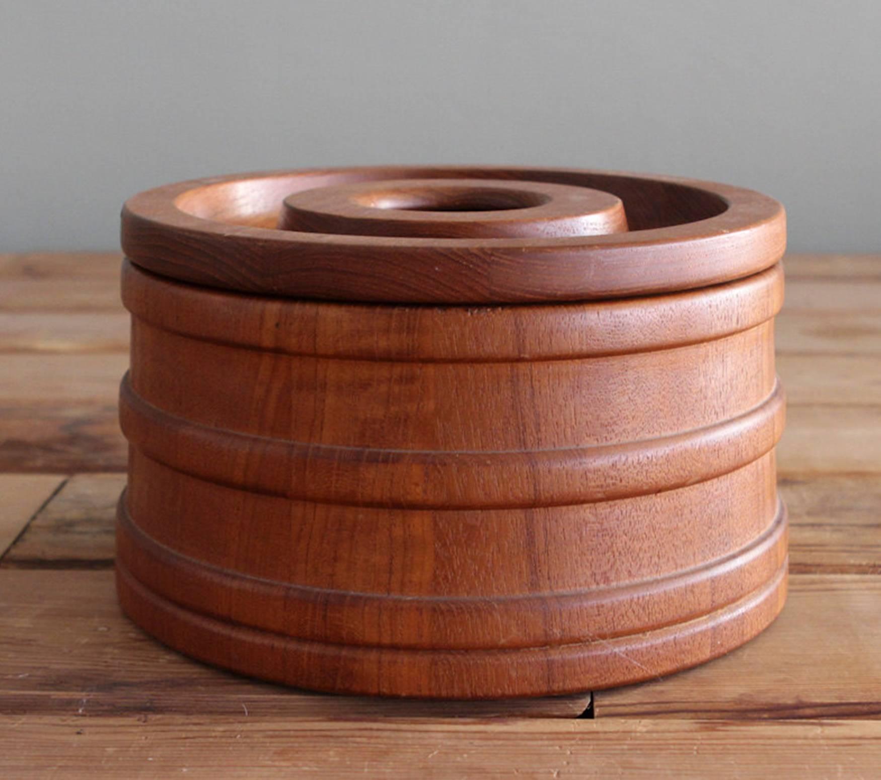 This staved teak lidded ice bucket was designed by Jens Quistgaard for Dansk. The container is a slightly tapered cylinder banded with rings and the lid has an integral handle. Retains its original black plastic liner

Measures 5 1/4 inches high