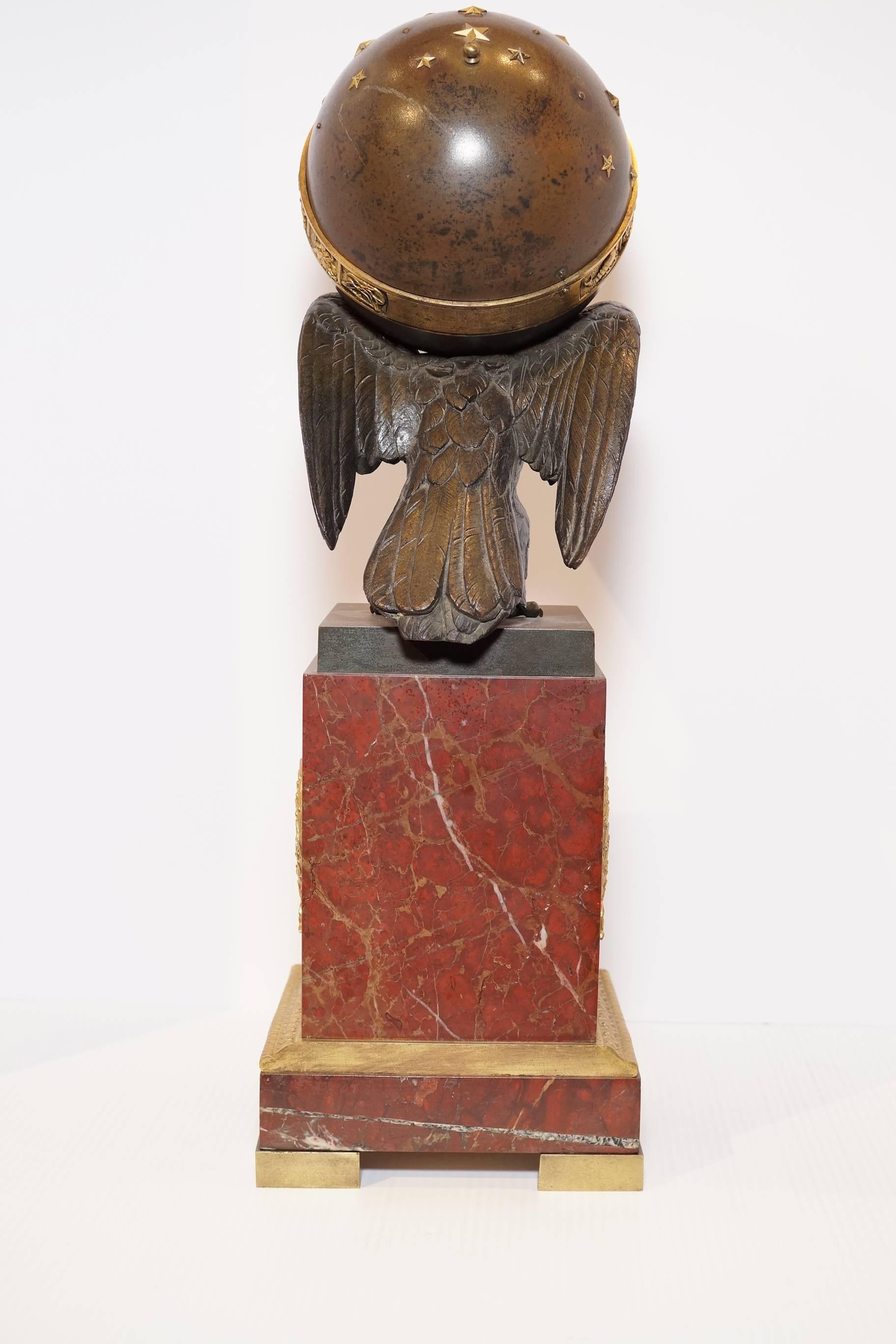 Very fine quality French Empire two tone gilt and patinated bronze clock depicting an eagle perching on a globe with zodiac signs sitting on a rouge marble base flanked by a bronze code of arms.