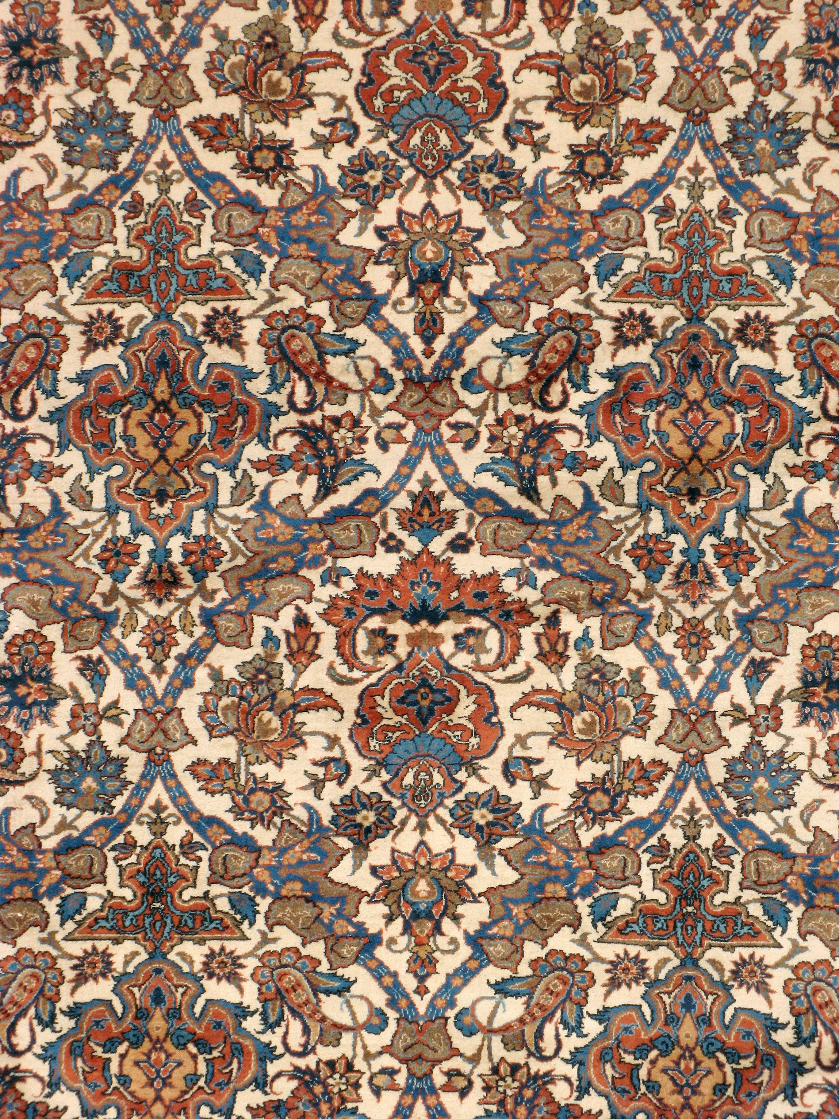 A vintage Persian Isfahan carpet from the mid-20th century with an intricate all-over motif. The pattern is symmetrical in one direction with blue, red and orange hues over an ivory background, bordered by a complex vine and scroll design.