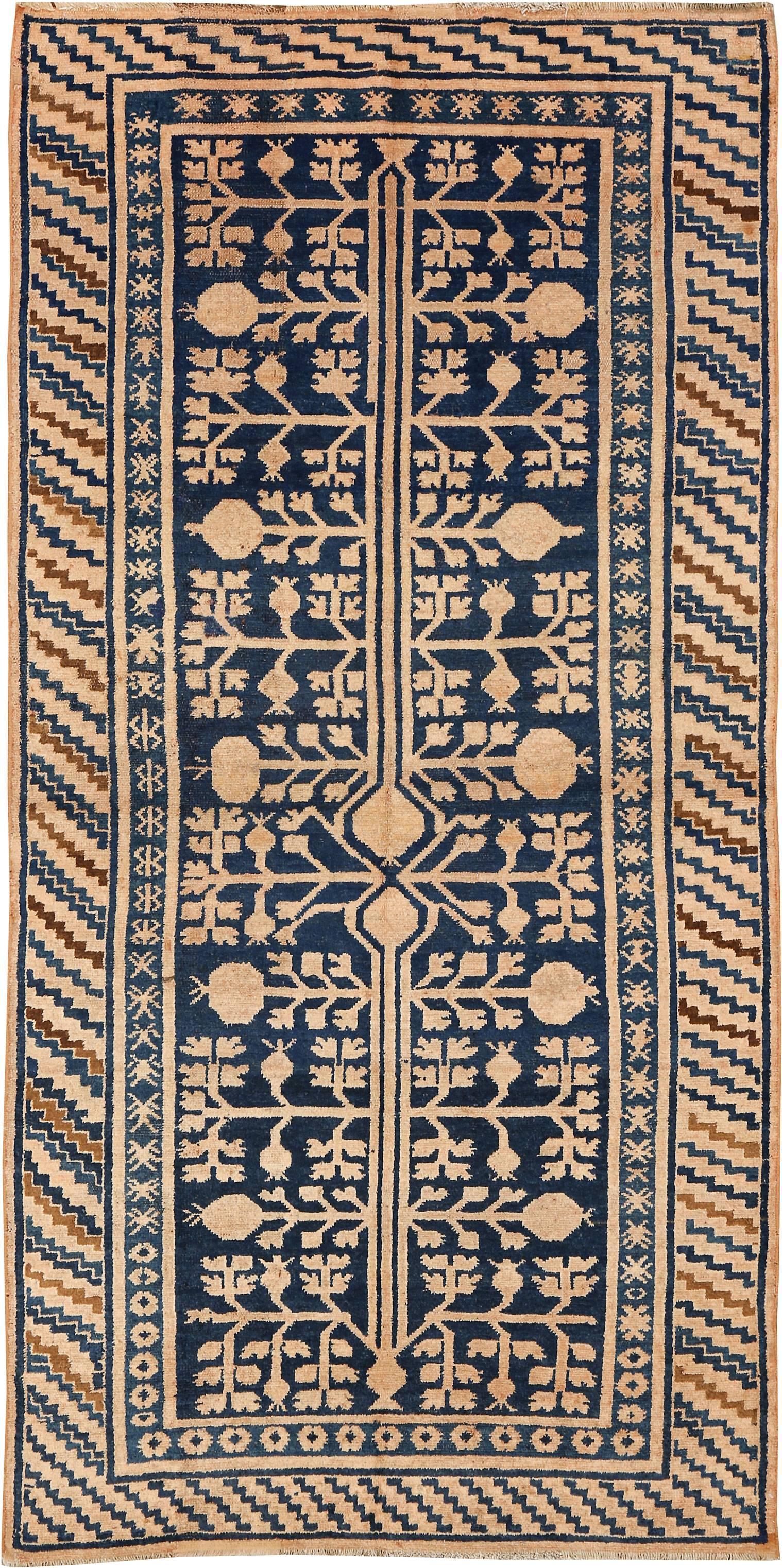 An antique East Turkestan Kirghiz carpet from the second quarter of the 20th century with a pomegranate design in camel and light terra cotta hues atop a navy background.