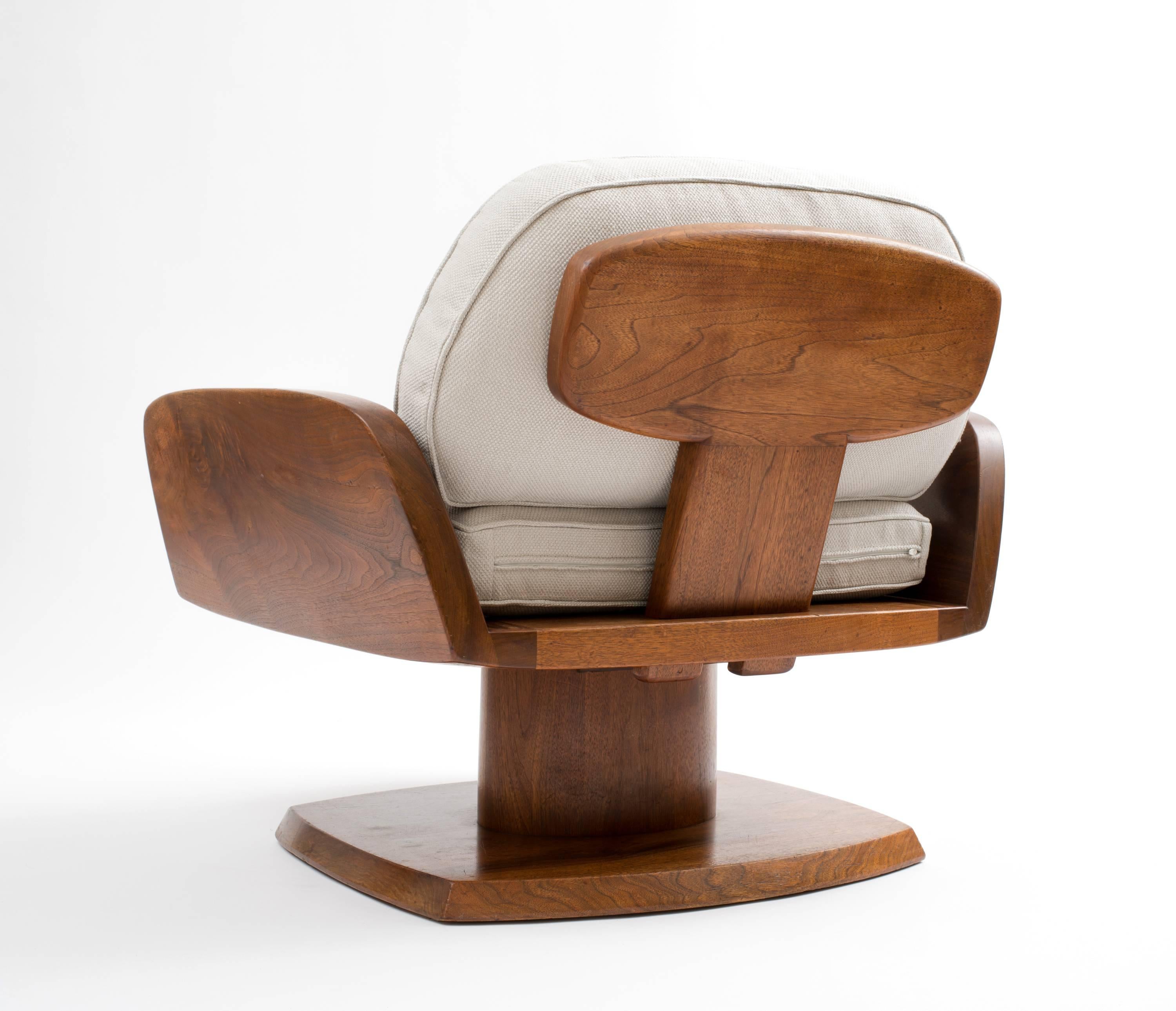 A modernist, upholstered lounge chair comprising a solid American Black Walnut frame, with a floating seat supported by a stationary pedestal base, and an ingeniously designed backrest that sets into the seat via two integrated 'pins', designed by