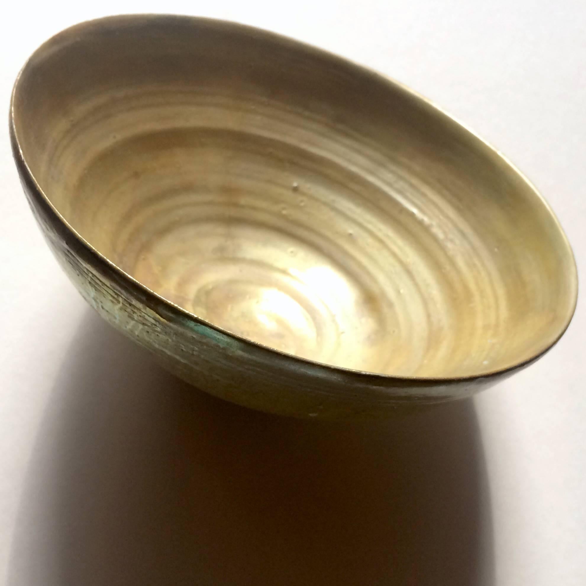 A striking example of Wood's famous lusterware, this iridescent gold bowl is a alluring contrast of primitive form and luxurious finish with beautiful variations in its shading and textures, accented by scattered drip lines and pooling. Dates to
