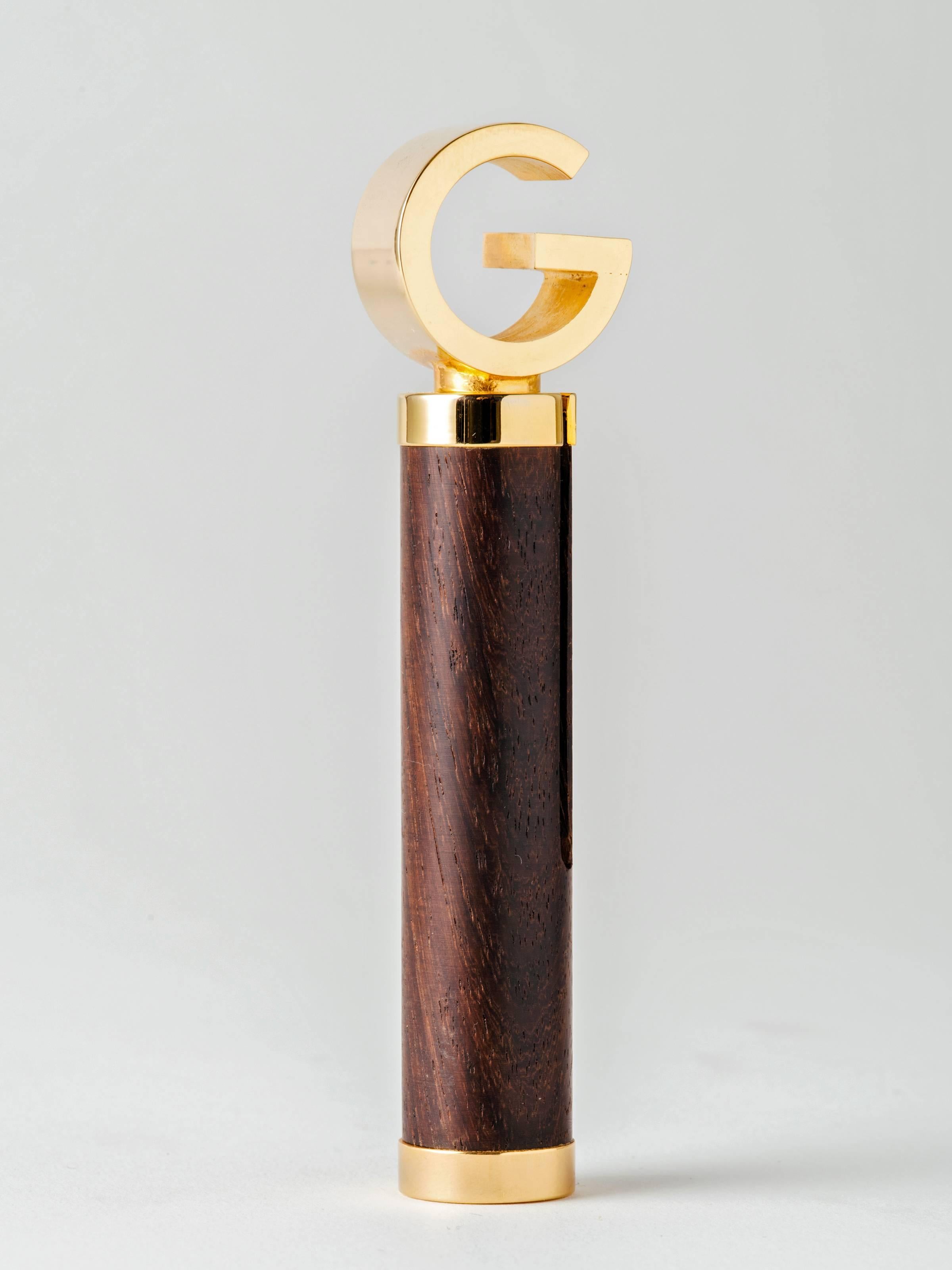 An ingeniously-designed, roundlet-style corkscrew or bottle opener executed in exotic wood and gold plated brass by Gucci, Italy, 1960s. The luxury brand's iconic G logo unscrews from the wood cylinder and slides precisely over one end to form a T