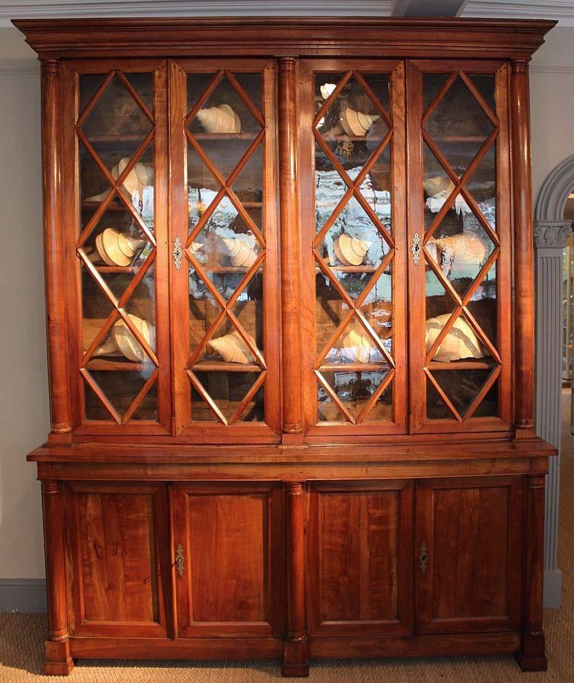 A fine early 19th century large French bookcase (or deux corps bibliotheque), of cherry wood, retaining the original glass panels. Wonderful color and patina. 
Featuring an upper tier with crown moulding, over two enclosed cabinets flanked by three