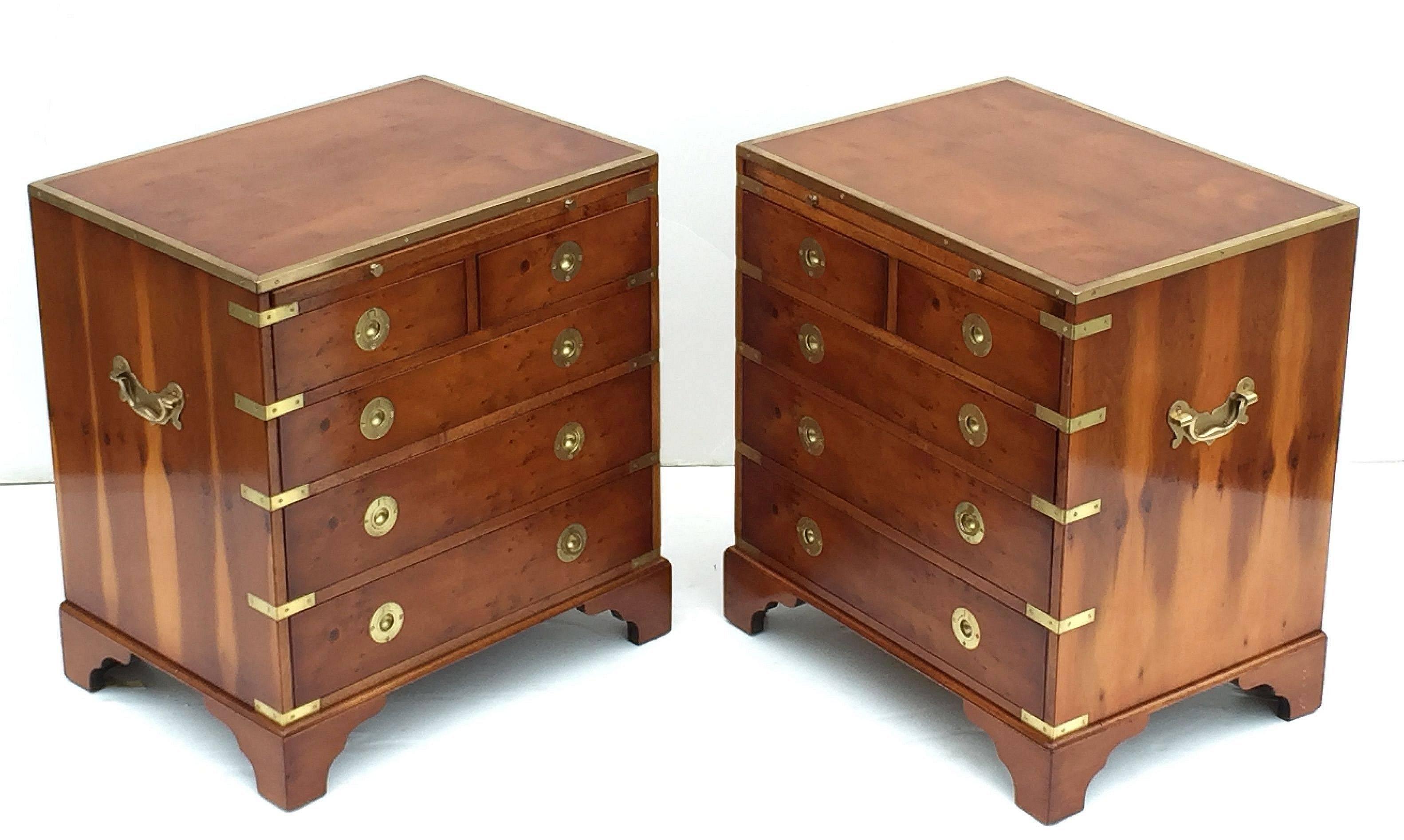 A fine pair of English nightstands or small side chests in the Campaign style, each chest featuring a brass-bound wood top and figured wood sides, with heavy brass hardware, the face with slide of embossed green leather, over two short drawers and