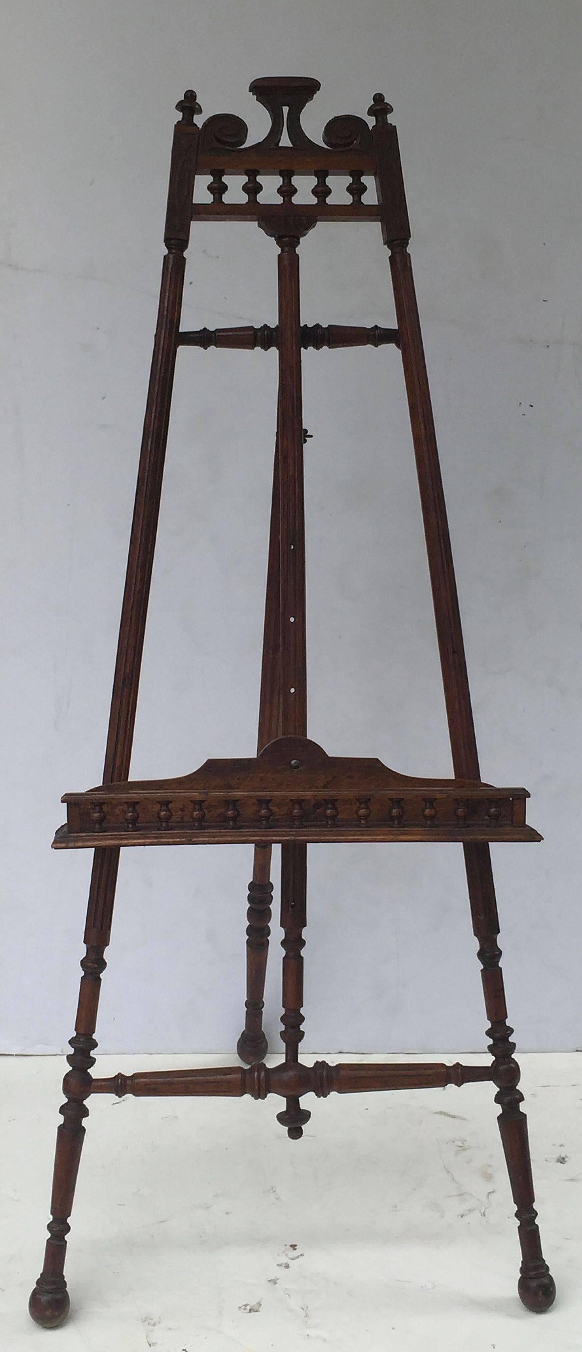 A handsome French display easel of oak, featuring a decorative top rail with a design of scrolls and turned spindles, adjustable canvas holder and tray with turned spindle gallery, and adjustable reeded support rails of turned wood and brass.