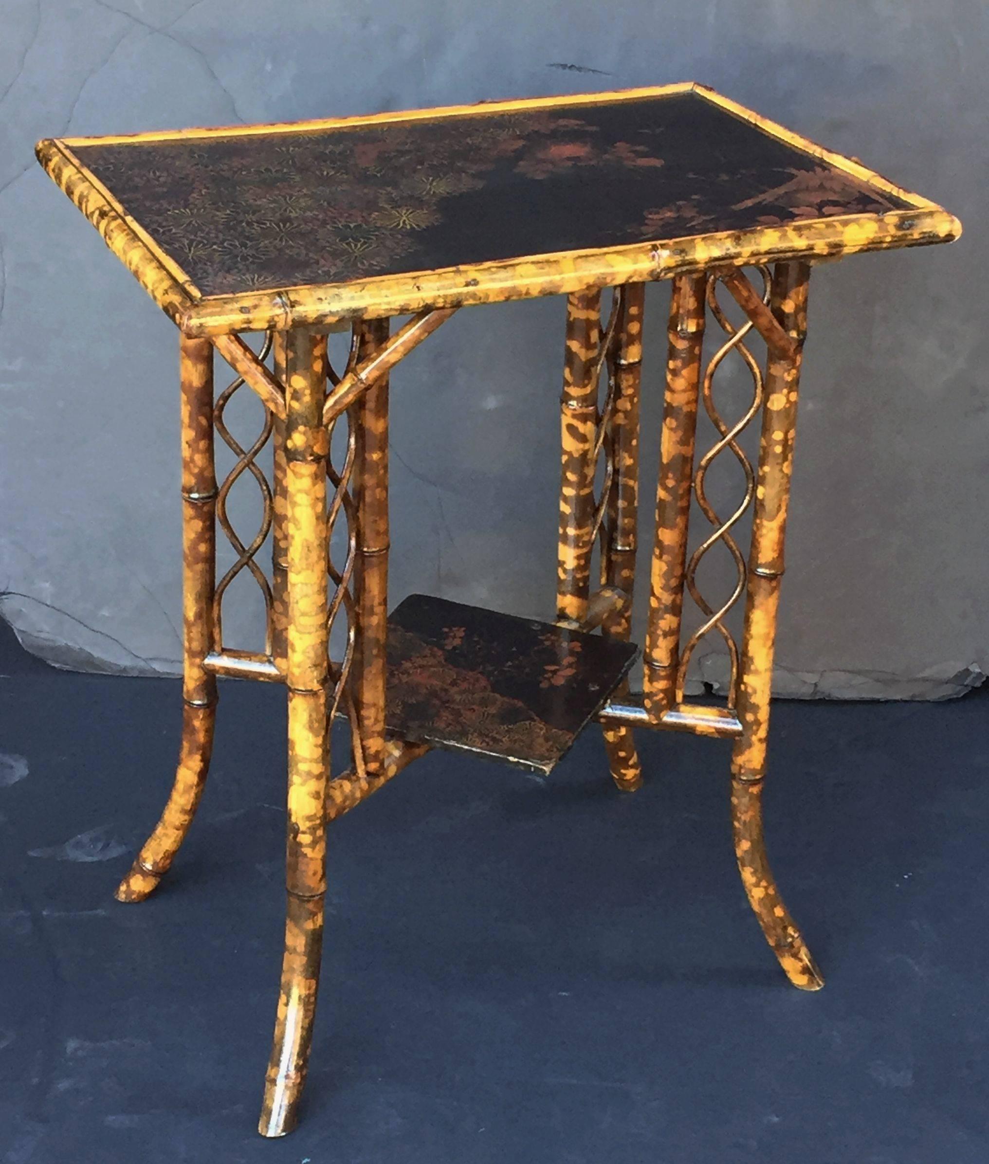 A fine English bamboo table featuring a rectangular top with Japan lacquered Chinoiserie design, over a stretcher base with square lacquered panel and ornamental serpentine fretwork running vertically at each corner.