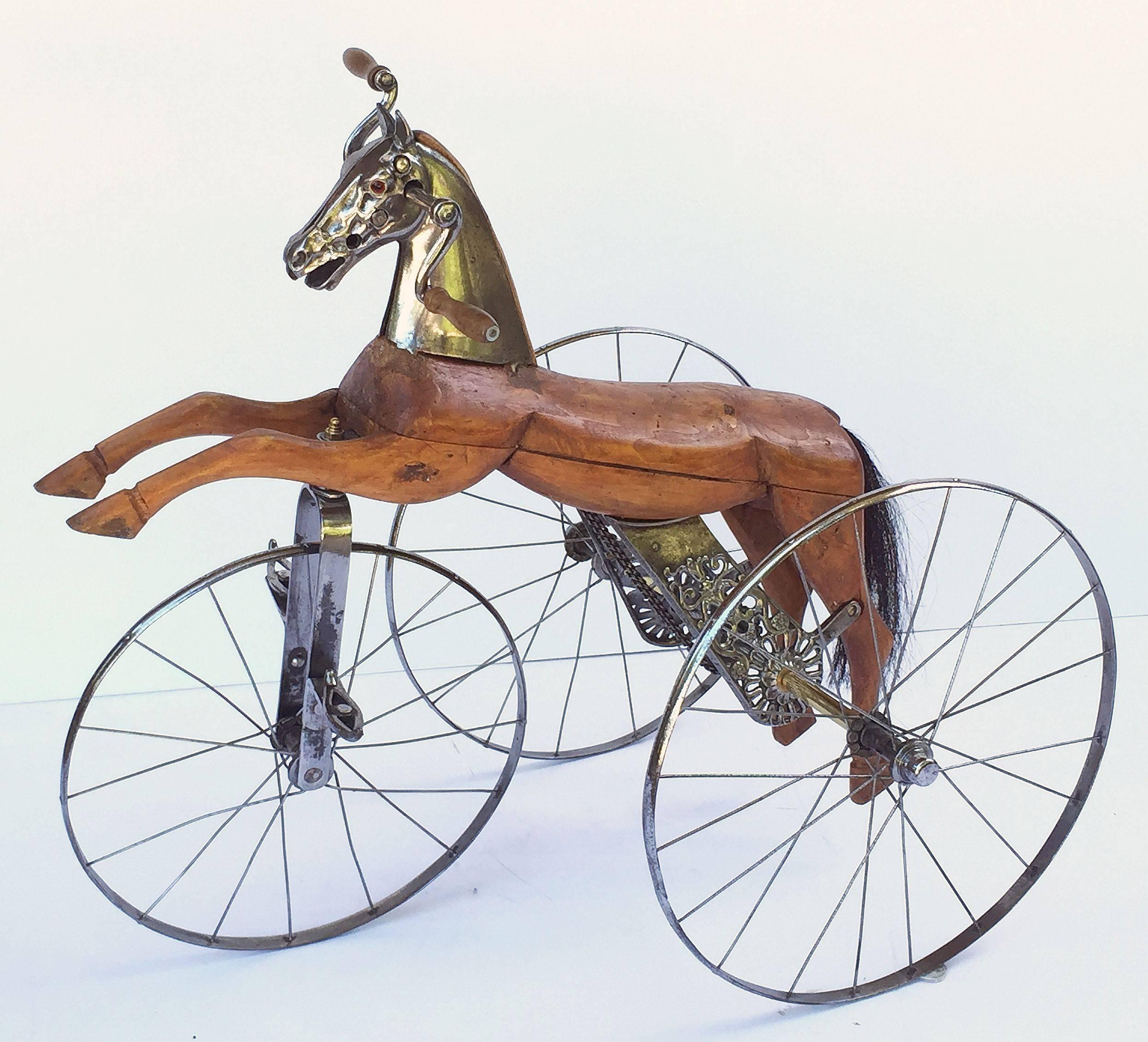 A 19th century French velocipede or child's toy horse tricycle featuring a body of carved wood with brushed steel face-plate and glass eyes, resting on spoke wheels with brass accoutrements and horse-hair tail.

A handsome objet d'art similar to