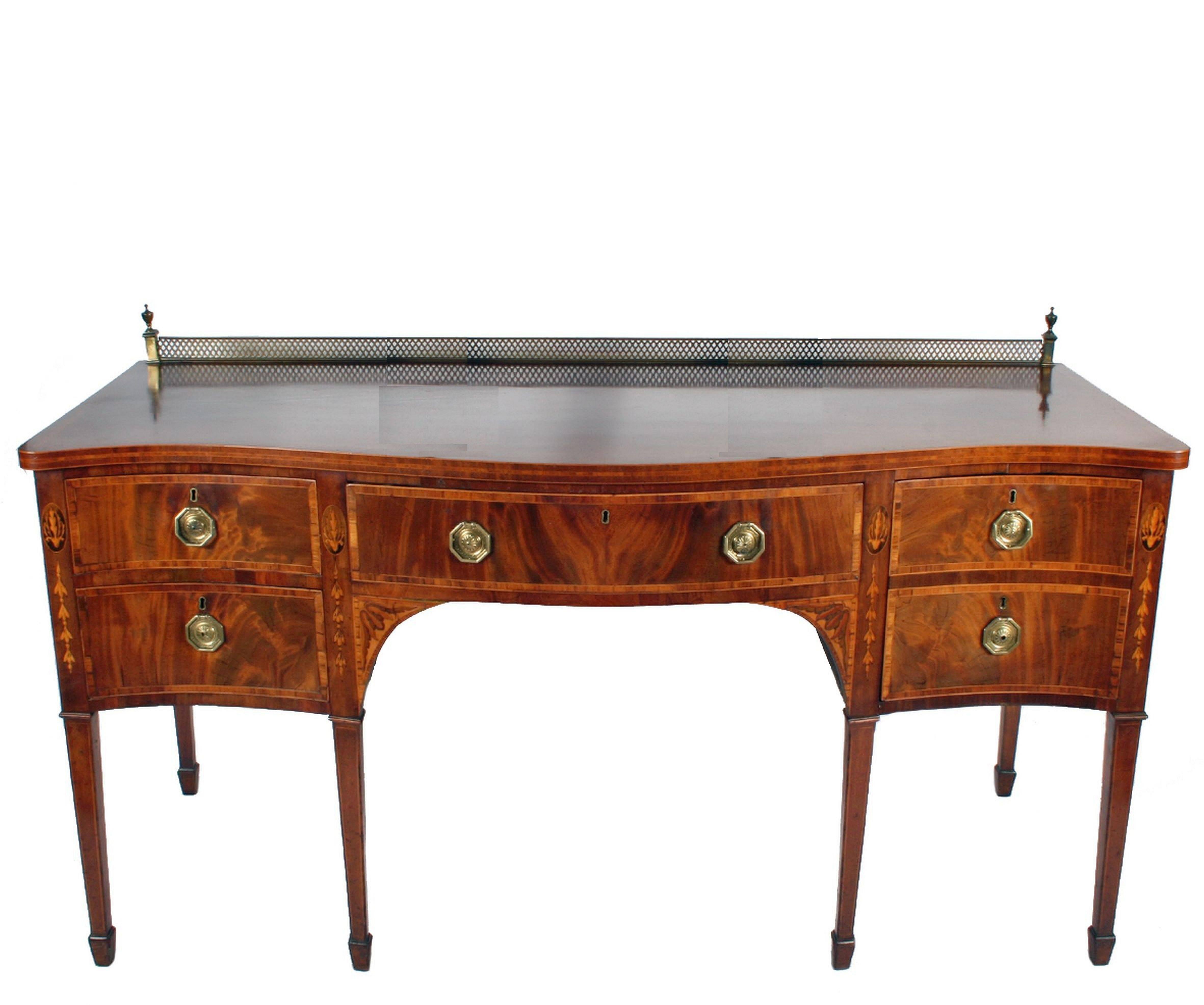 A handsome English sideboard server (or serving console) from the Georgian era, featuring a serpentine moulded top with pierced brass back rail with urn finials, over an inlaid mahogany frieze with two left-facing small drawers, bowed middle large
