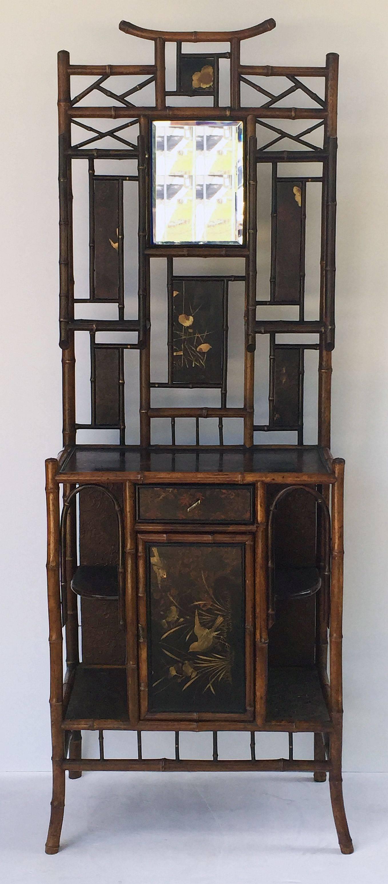 A large English bamboo cabinet featuring an upper tier with an Aesthetic Movement design of lacquered panels and fretwork surrounding a rectangular beveled mirror, over a cabinet lower tier with Japan lacquered top and embossed paper sides, over a