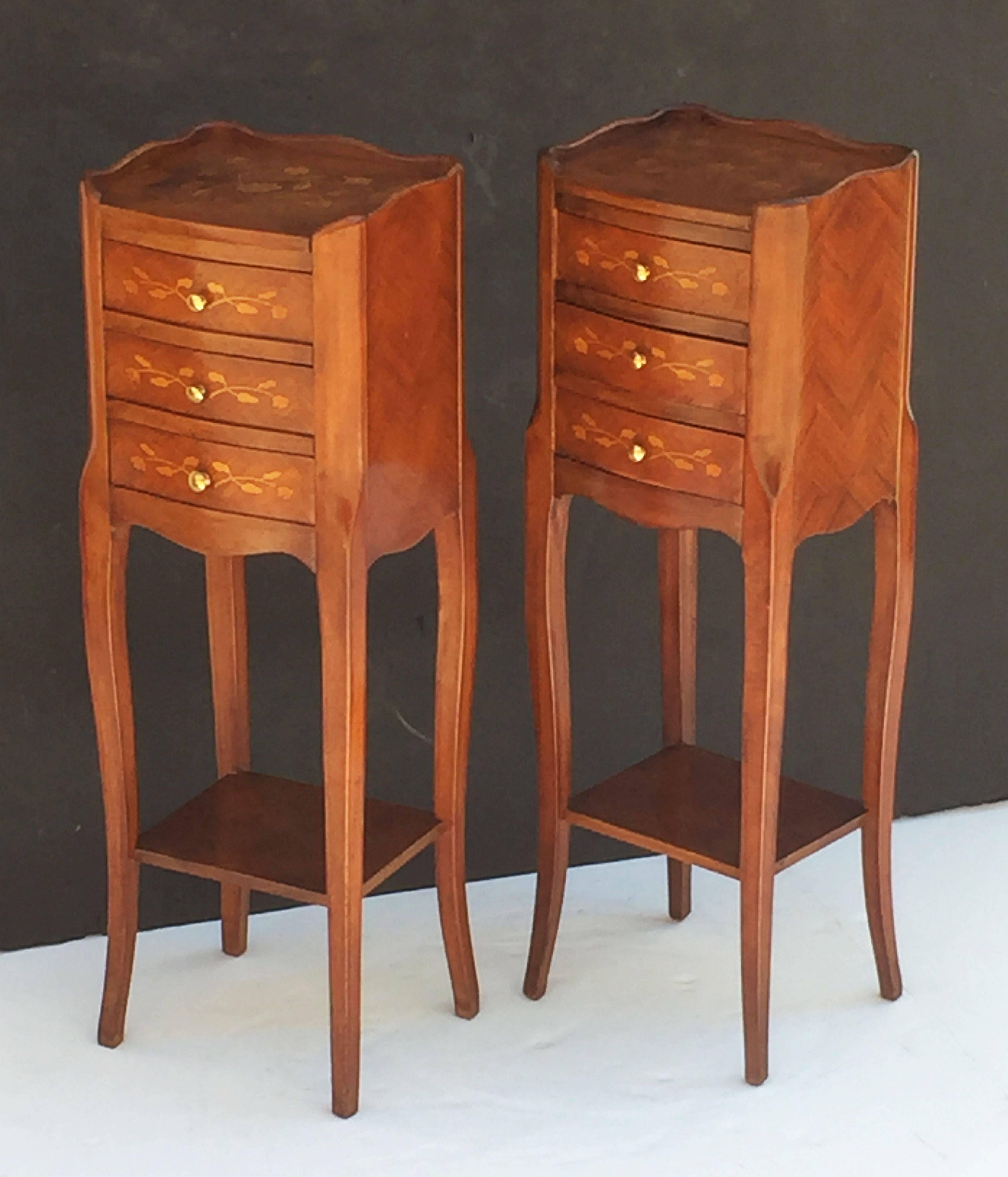 A fine pair of French bedside tables or nightstands, each stand featuring an inlaid top with serpentine gallery over a frieze of three inlaid drawers with brass pulls, marquetry sides and apron bottom, set upon four cabriole legs and stretcher