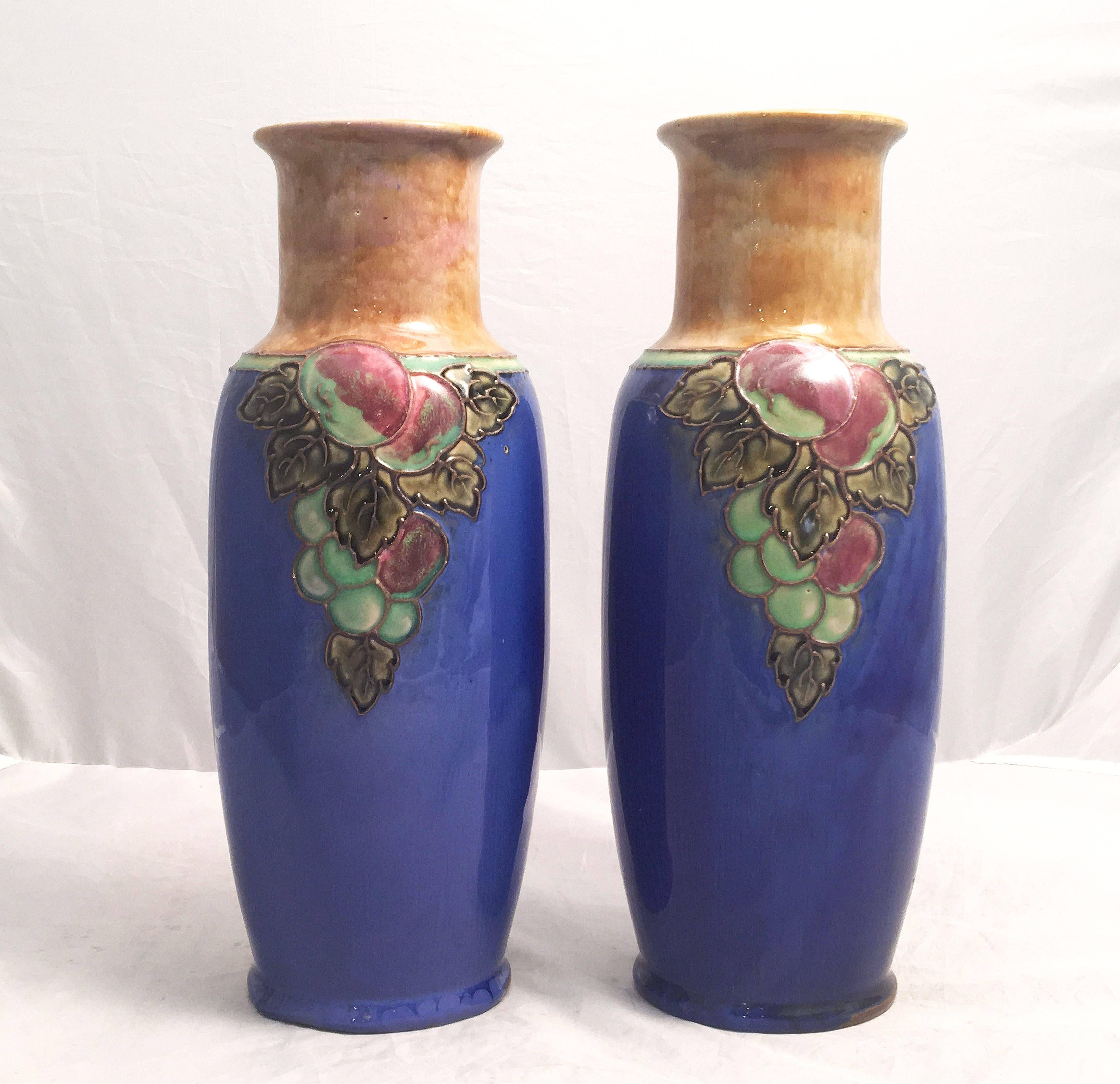 Une belle paire de vases décoratifs en céramique de la période Arts & Crafts, par la célèbre entreprise de poterie anglaise, Royal Doulton.

Chaque vase présente un motif de grappes de raisin sur le pourtour. Marque imprimée à la base.

Deux