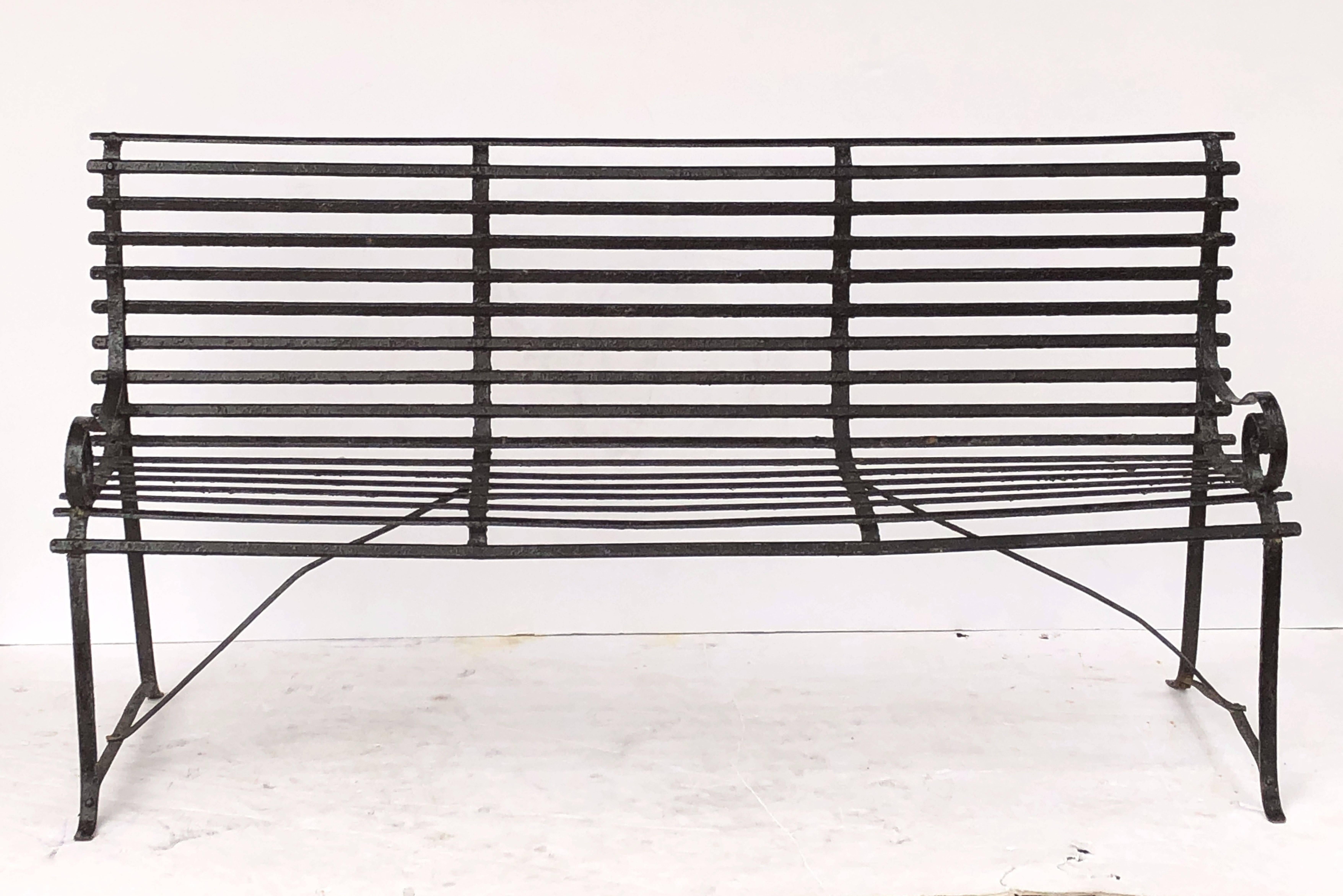 A fine American garden seating bench (or garden seat) of painted iron, featuring a comfortable back and seat with a graceful curvature and serpentine arms, set upon a stretcher base support with four legs.