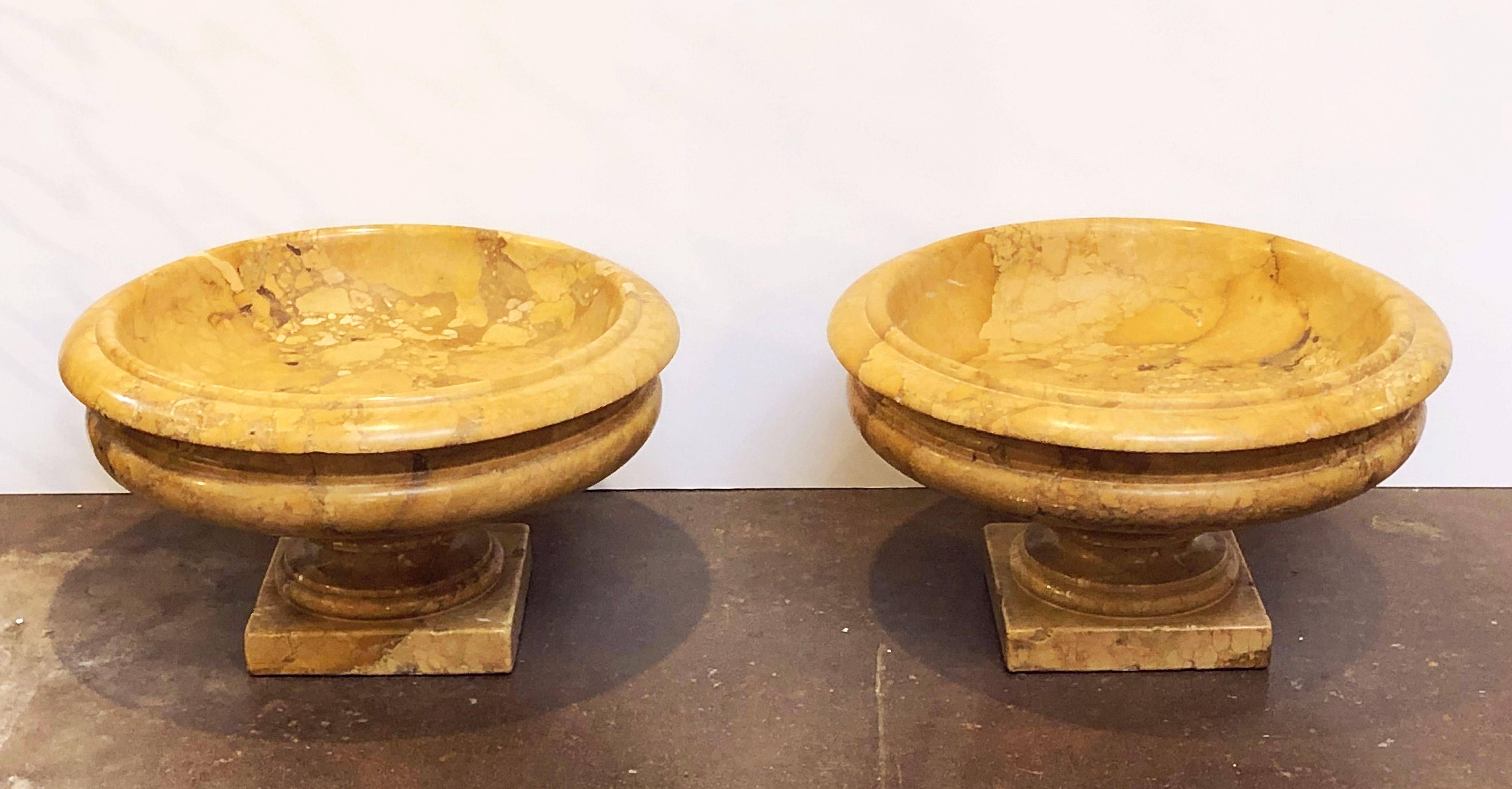A lovely pair of large Italian urns or planter pots of carved Siena marble in the Neoclassical style, each urn featuring a rolled top edge over a round basin bowl and set upon a footed square plinth base.

A magnificent addition to an indoor or