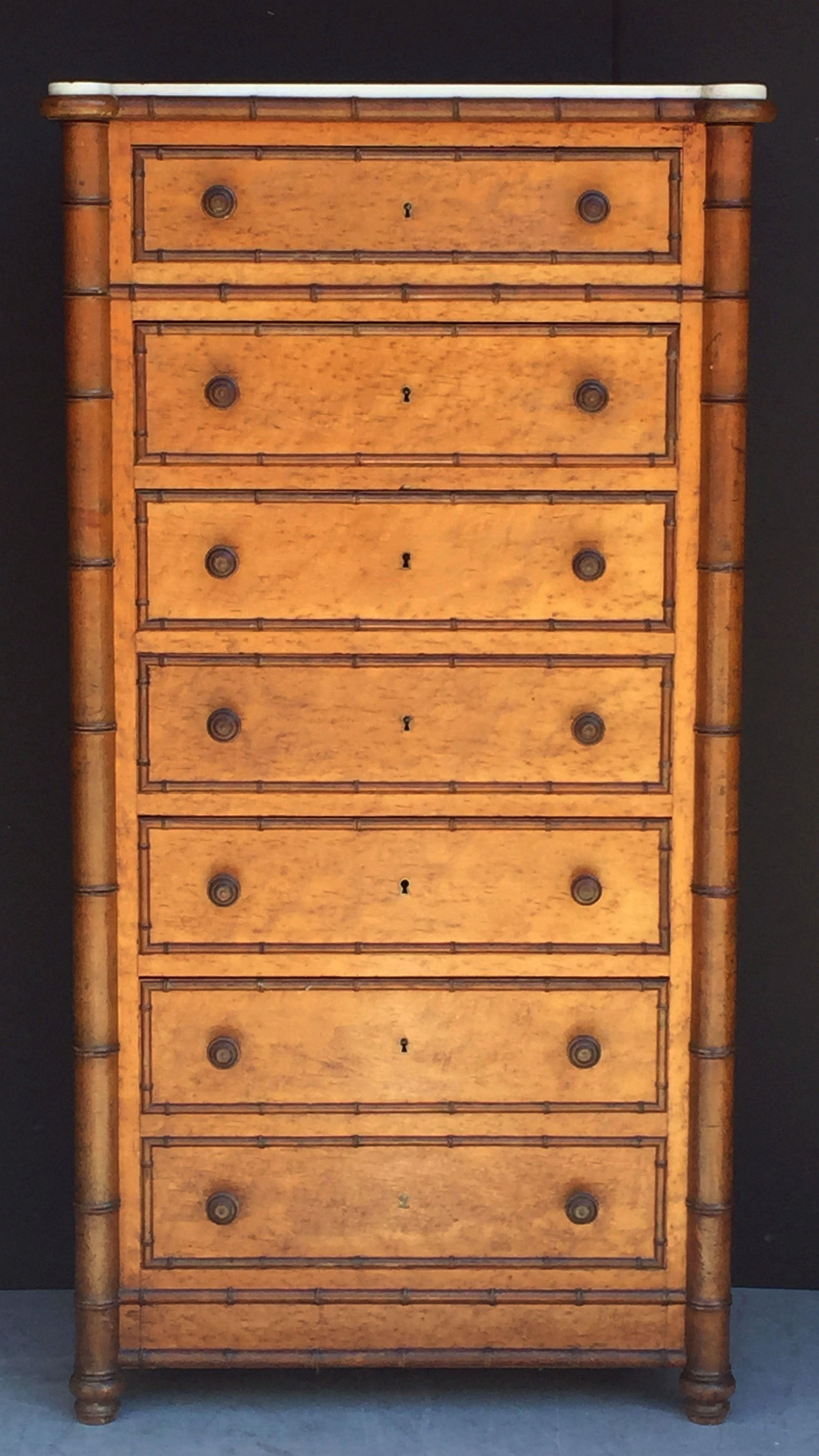 A fine French semainier collector's cabinet or chest of faux bamboo and figured curly or bird's-eye maple, fondly known as a Wellington in England, featuring a marble top over seven drawers, with decorative faux bamboo accents, turned knobs, and