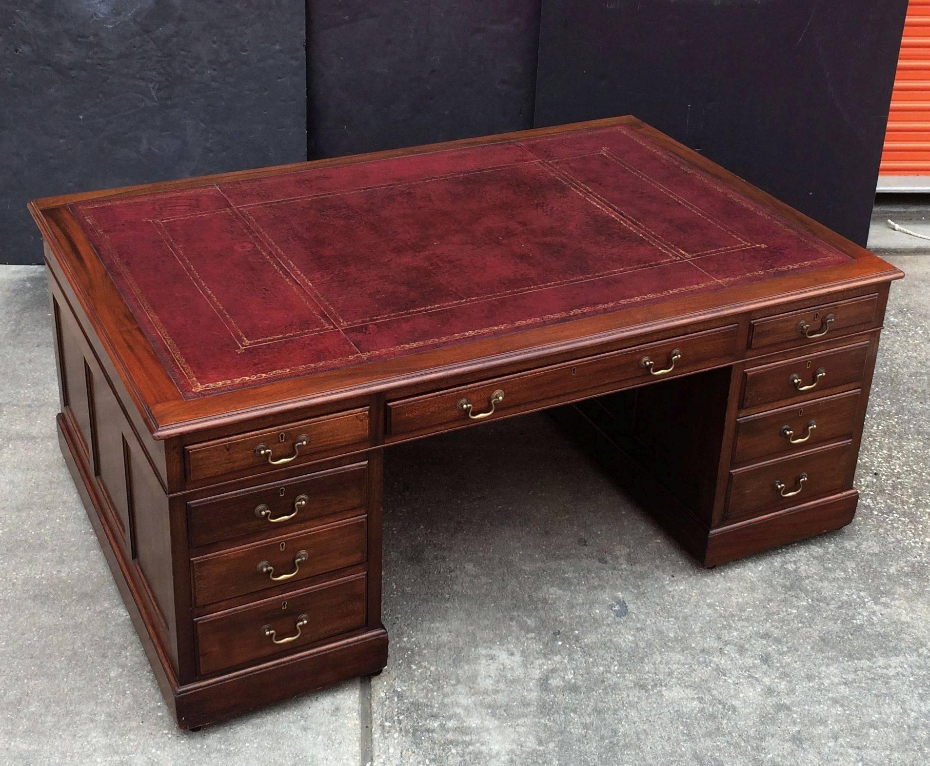 A fine large English partner's desk of mahogany, featuring a moulded top inset with a handsome gilt embossed red leather, over a long drawer flanked by two short drawers on opposing sides. 
One pedestal with three short drawers resting on raised