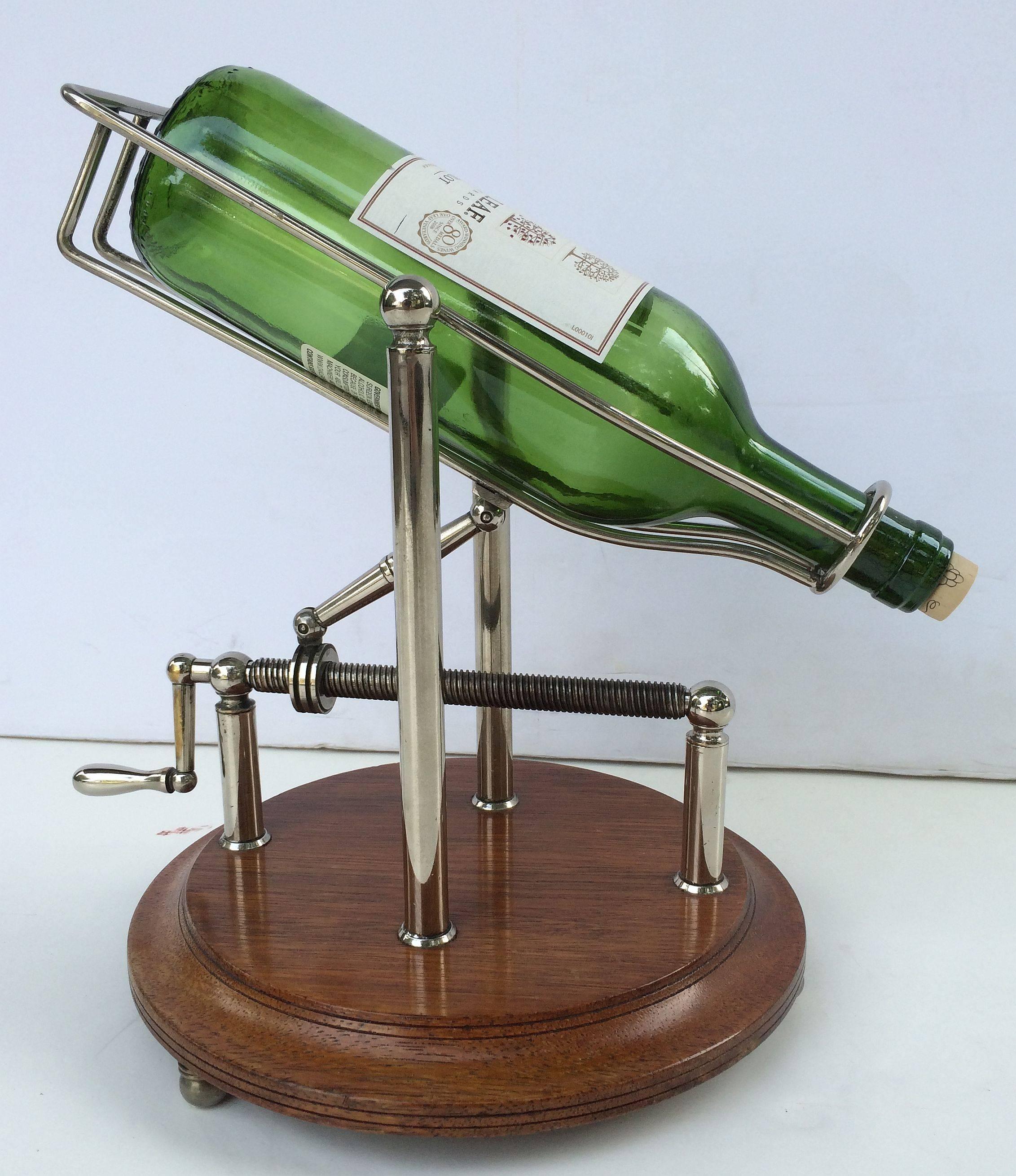 A handsome English port or wine bottle pourer of chromed brass with turn screw action, on moulded round wooden base with three knob feet.

A mechanical spirits pourer or decanting cradle is an artisan-like decanting device. Turning the screw
