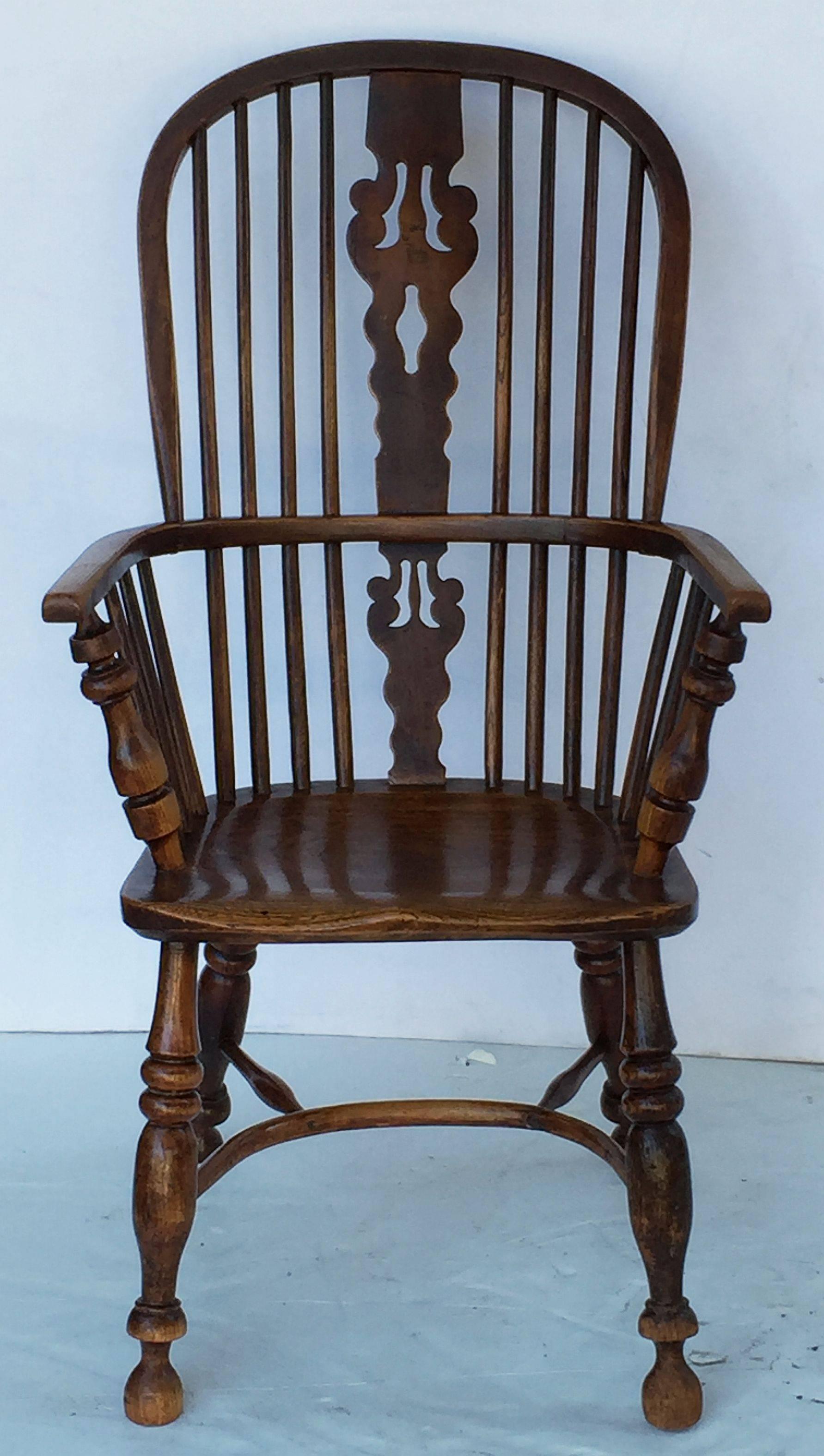 A handsome large English Windsor high back chair of elm and ashwoods, featuring a bowed top rail and pierced splat and spindle back, with solid seat on turned crinoline stretcher. With a scroll-work design to the split.