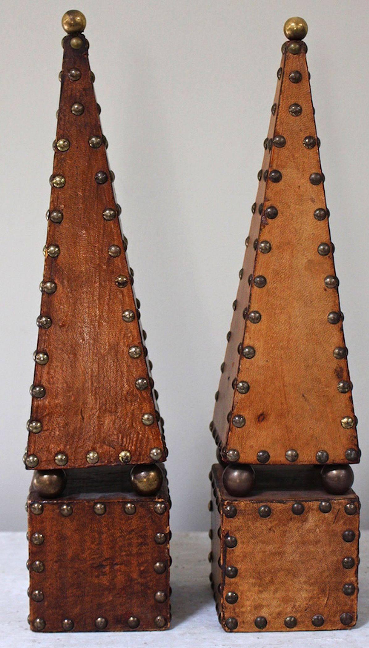A fine pair of English decorative obelisks or desk-top or mantle sculptures, in studded leather, each featuring a tall architectural pyramid obelisk set upon a square base, topped with a brass ball finial.

Priced as a pair - $2895 the pair