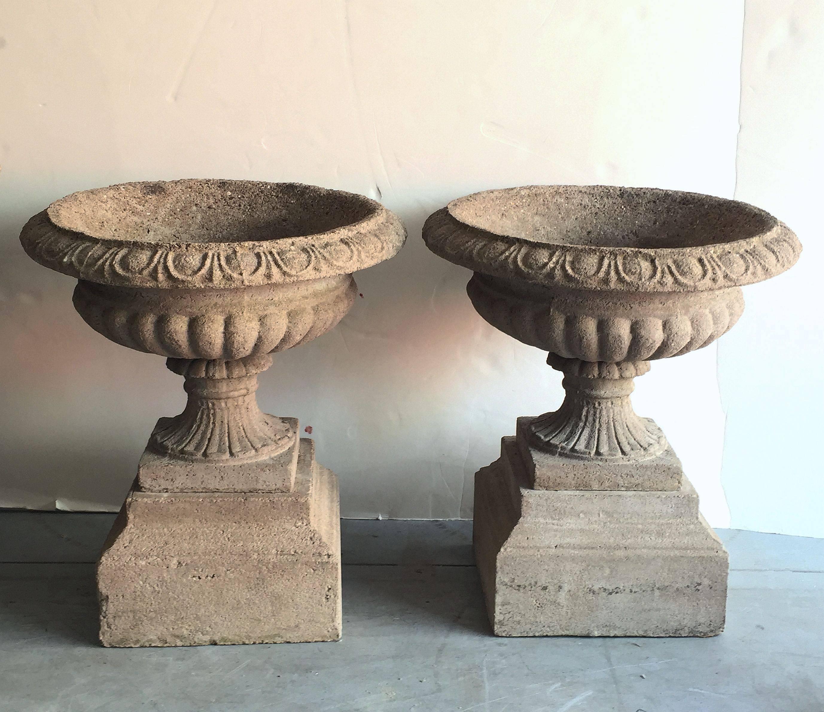 A fine pair of English garden urns (or planter pots) in the Classical style, of composition stone, on raised square plinths.
Each bowl featuring an egg-and-dart edge over a fluted column and square base, each set upon a graduated square plinth.

An