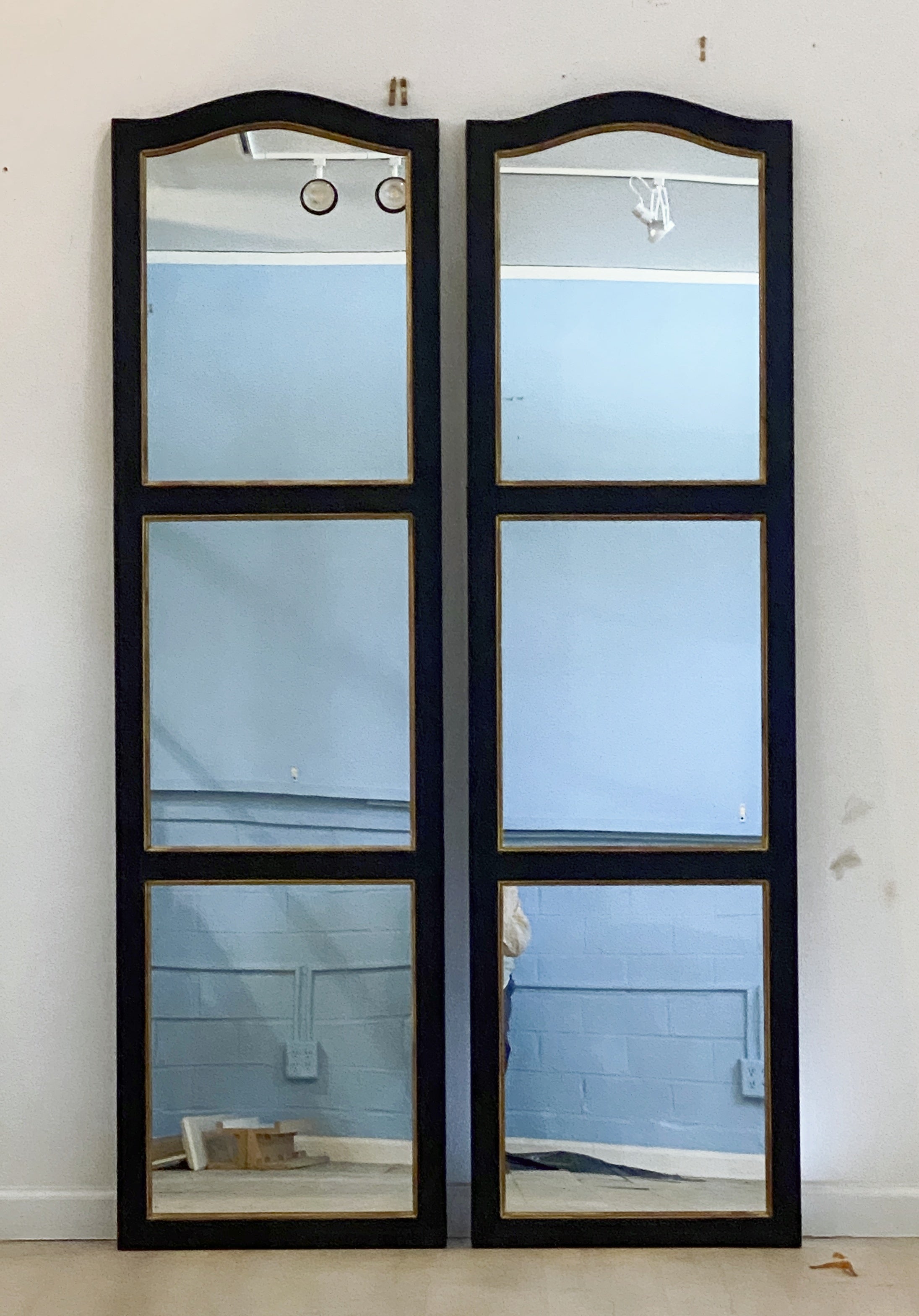 A handsome pair of large decorative window pane paneled mirrors from England - each mirror featuring an ebonized frame with gilt accents surrounding three panels with mirrored glass.

Each paneled mirror measures: H 74
