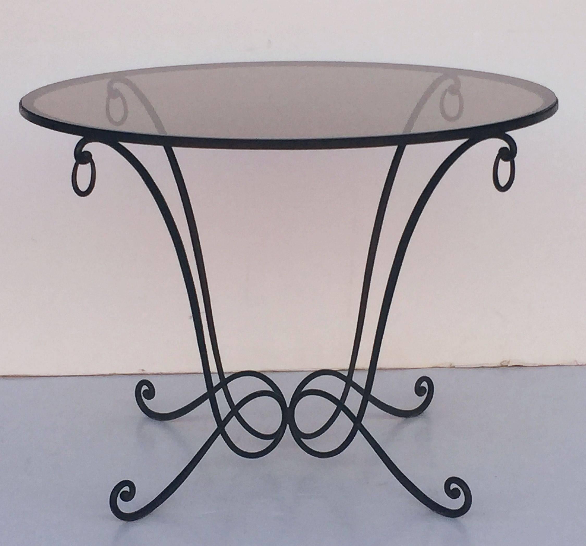 A fine French round table of wrought iron with a smoked glass circular top, featuring a design of four serpentine supports, ending in o-rings at top and scrolls at the base.

Can be used outdoors and indoors.
