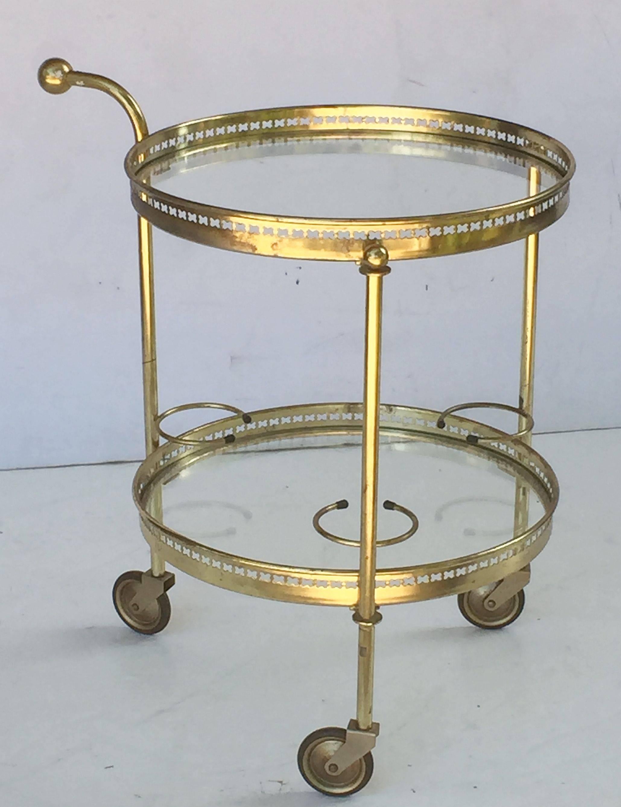 A fine French drinks cart table or trolley server (or bar cart) of brass and glass, featuring two round or circular glass tiers, each with pierced brass galleries, mounted to a tripod brass support with brass handle and rolling caster wheels.
The