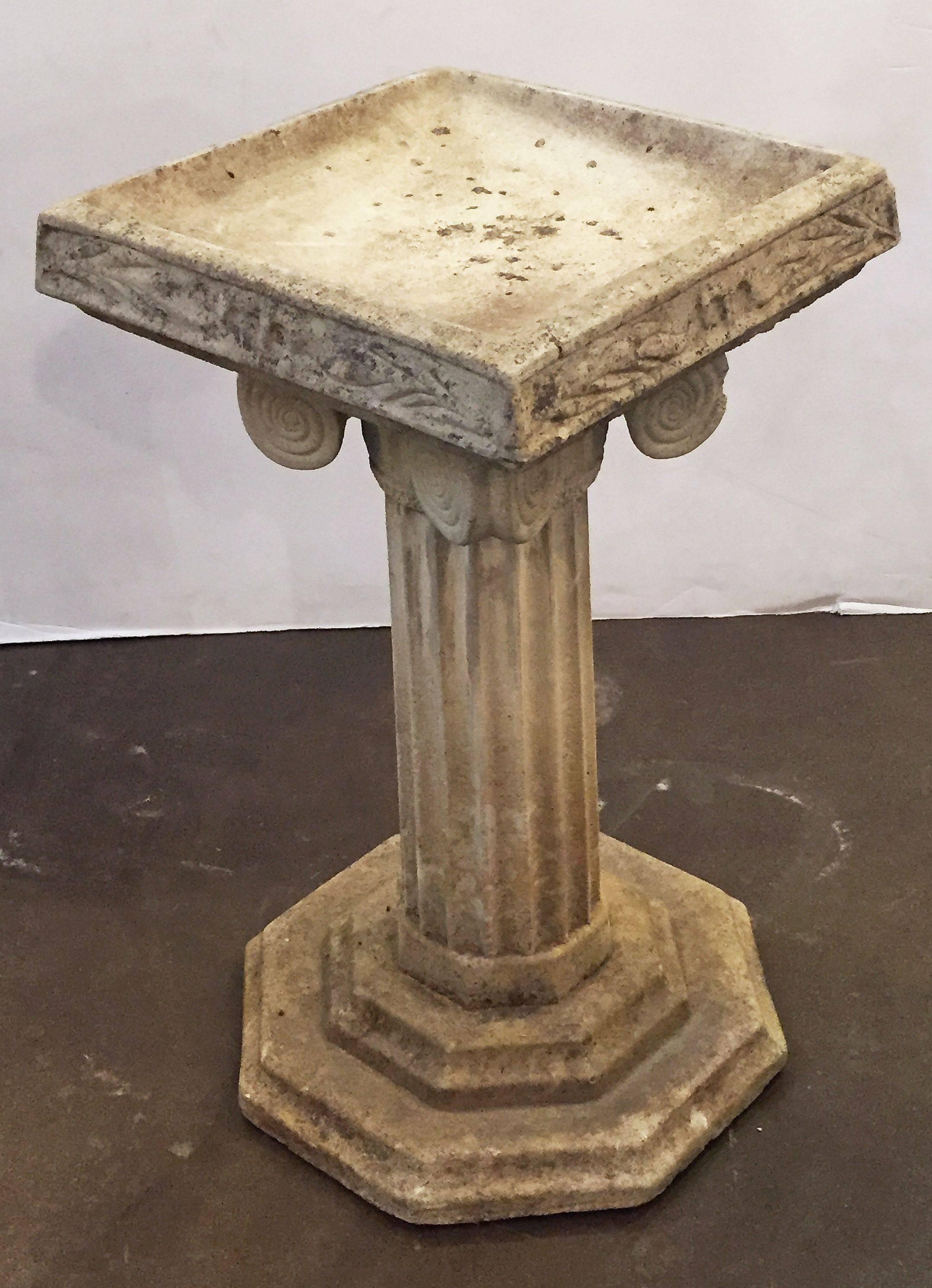 A fine English garden bird bath of weathered composition stone, featuring a square top with Classical relief design around the four sides, set upon a fluted Ionic column pedestal with scrolls or volutes and graduated octagonal plinth base.

Perfect