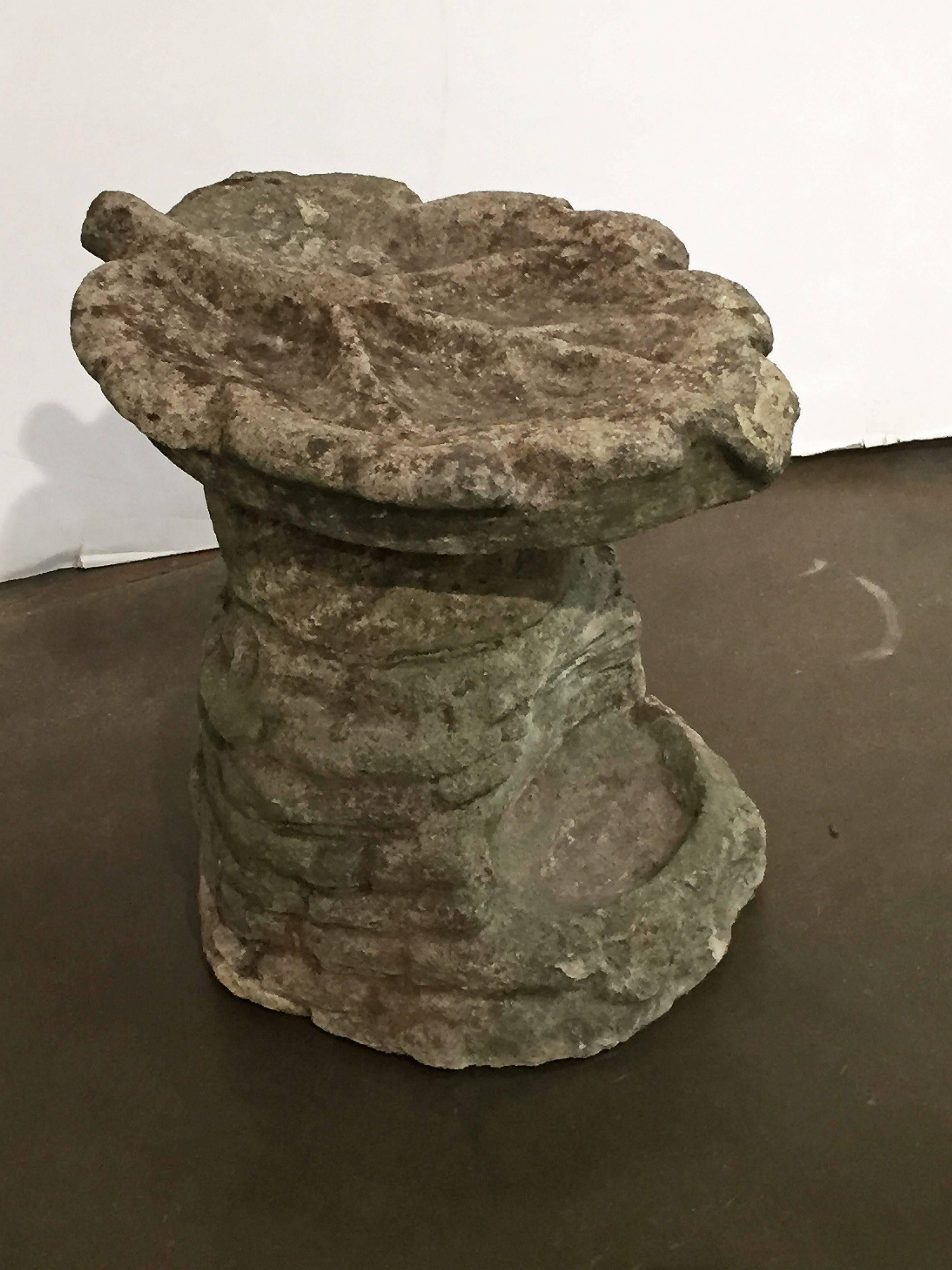 An English garden bird bath and feeder of weathered composition stone, featuring a removable top in the shape of a large oak leaf, set upon a base with a rock ledge design and recessed area for bird feed or water.