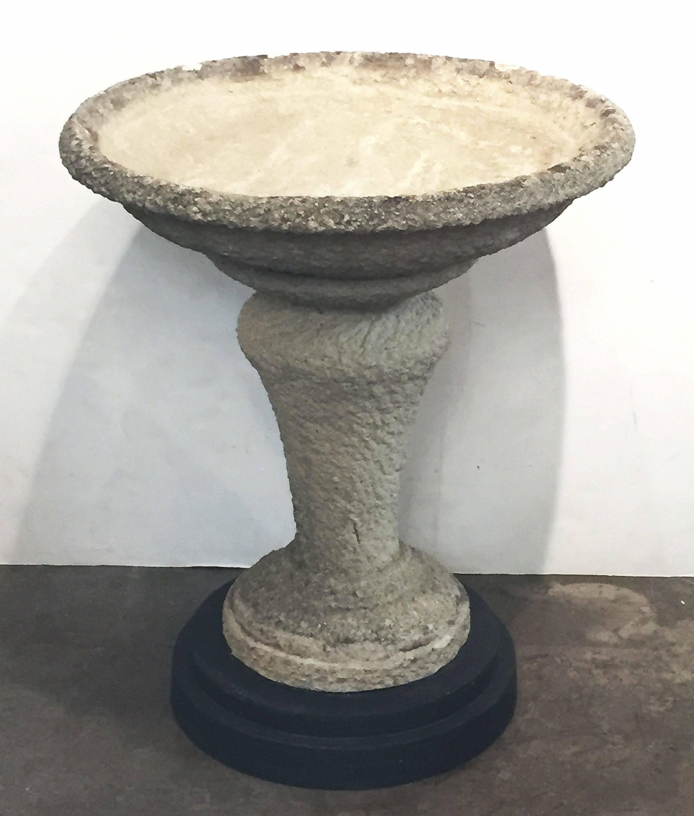 A large English decorative planter on stand of composition stone, featuring a large flared round basin top, set upon a pedestal stand and optional round ebonized wooden base. Can be plugged for use as a bird bath.

An excellent addition to an indoor