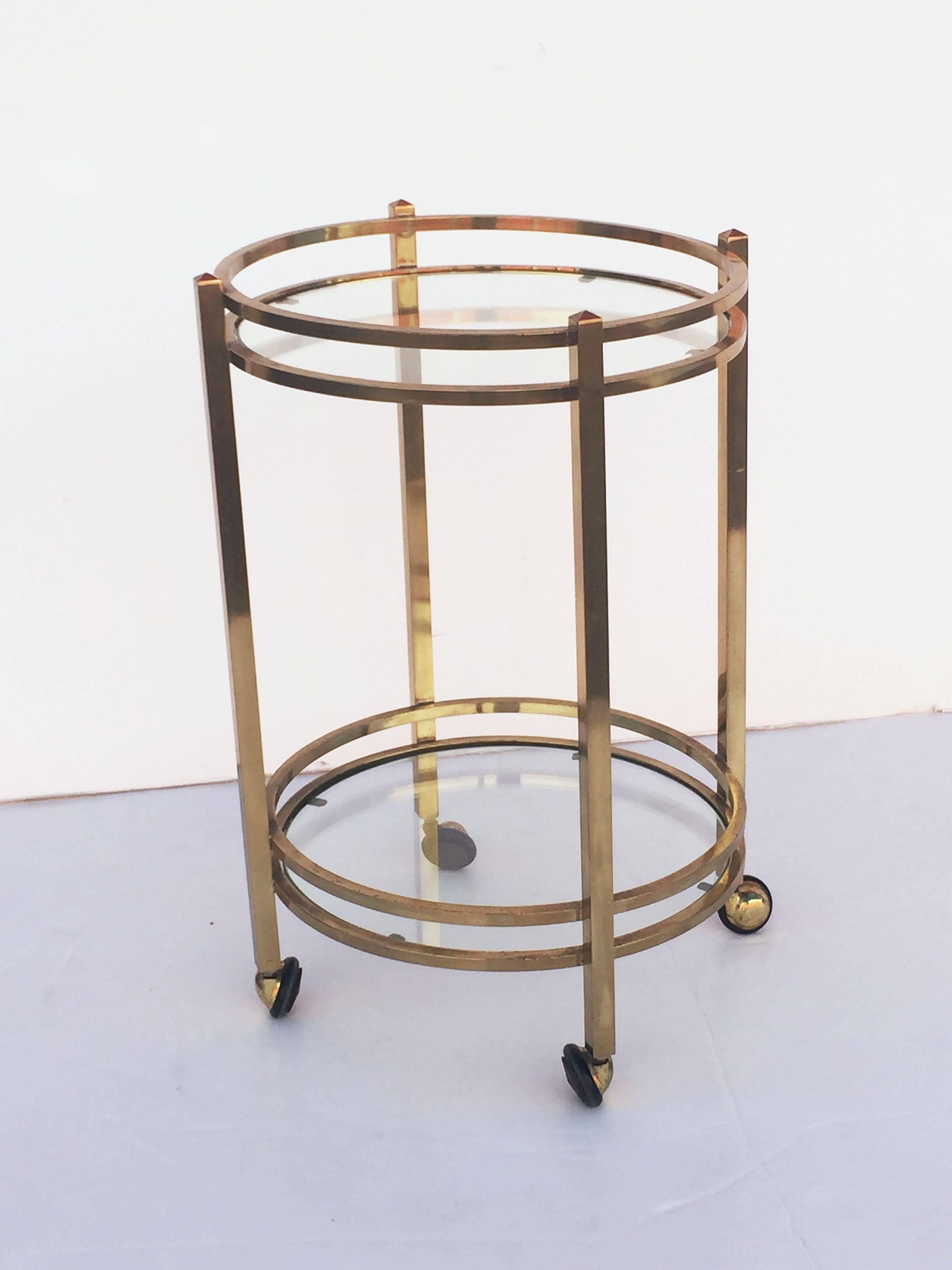 A fine French round table of brass with two concentric circle tiers of inset glass, set upon rolling casters.

Great as a drinks trolley or bar cart as well.