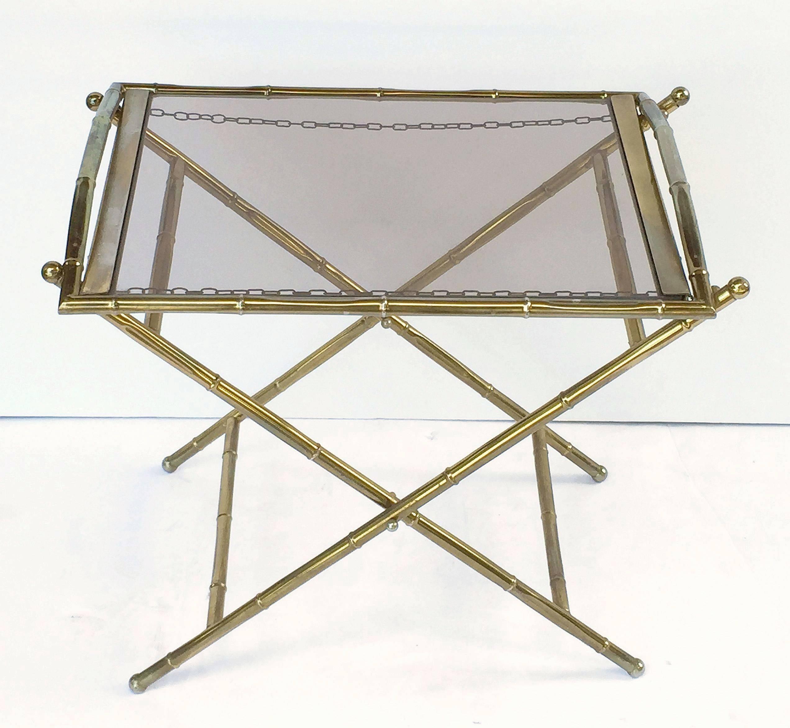 A fine French low or side tray table featuring a removable serving tray with a bamboo design in brass with inset smoked glass, set upon a folding stand.