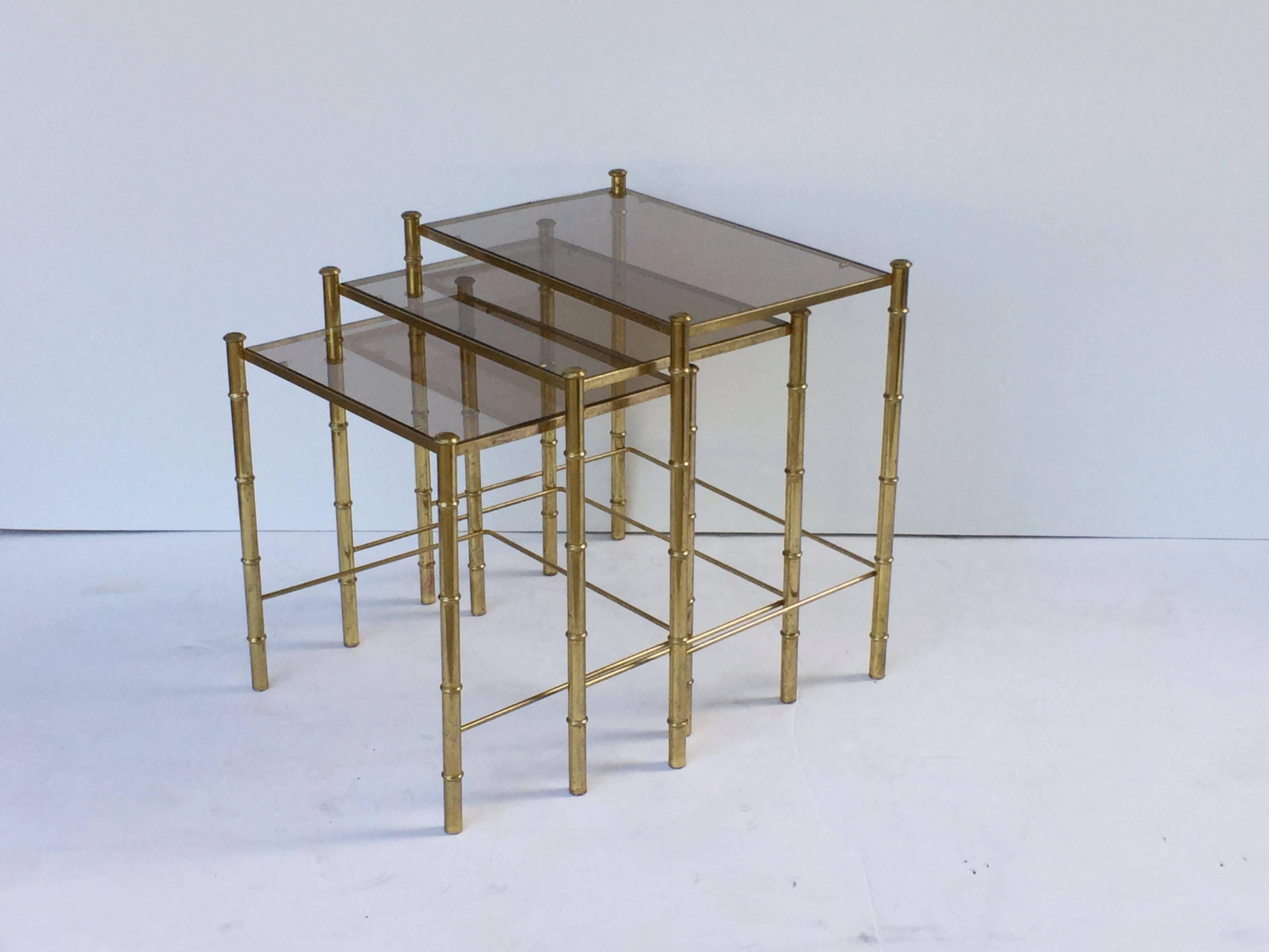 A set of French rectangular nesting low tables featuring three fitted tables, each with a faux bamboo design in gilt metal with inset rectangular smoked glass top.

Great for use as cocktail or coffee tables as well.

Measures:
Large table