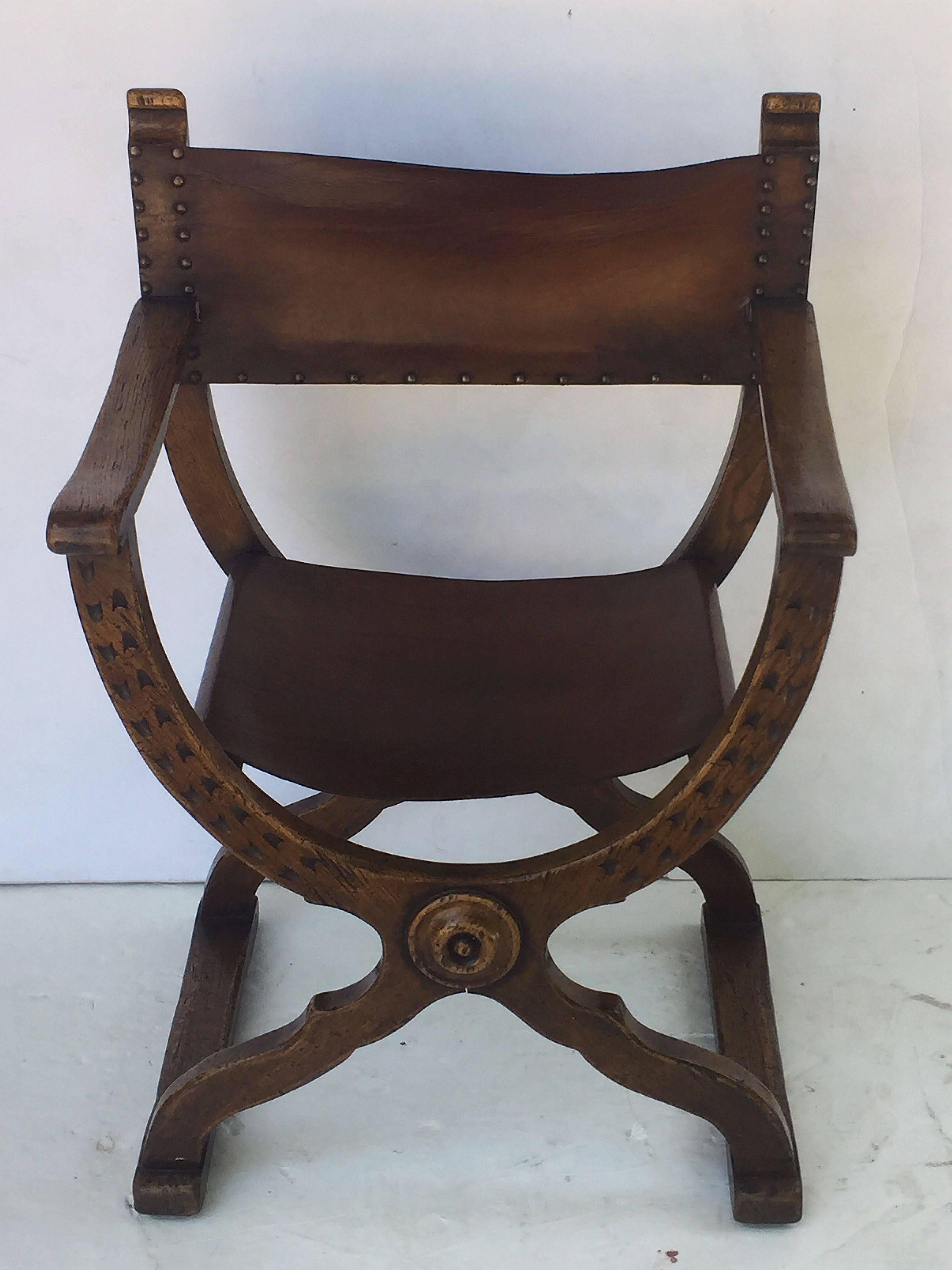 A comfortable Continental armchair (or lounge chair) in the X-shaped Roman style known as a Savonarola, featuring a finely patinated wooden body with aged leather back and sides and nail-head accents.