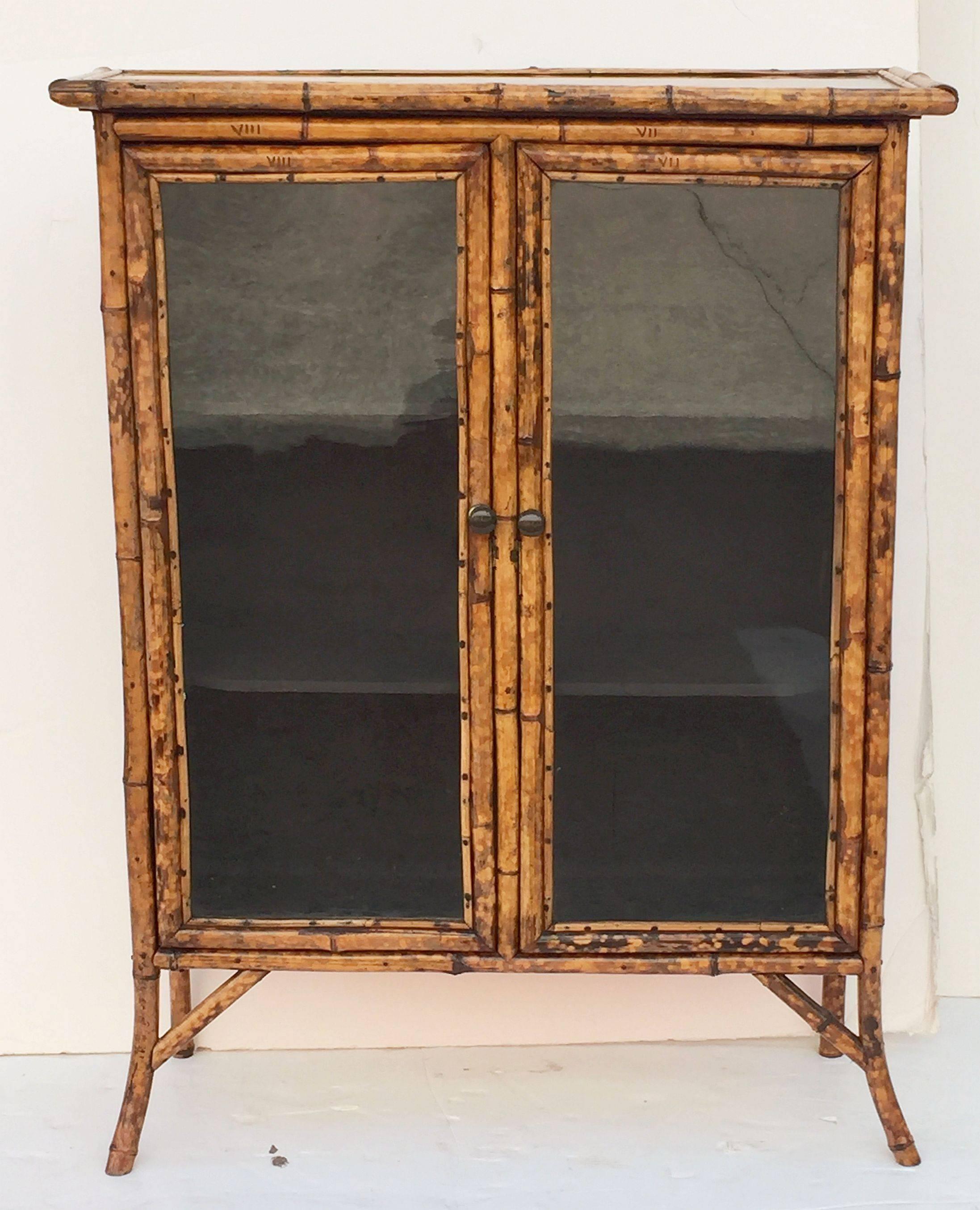 A handsome English bamboo bookcase, from the Aesthetic Movement era, featuring a japan-lacquered top with bamboo accents, over two framed-glass doors with brass hardware, opening to an interior of two shelves, each cabinet side exterior, lined with