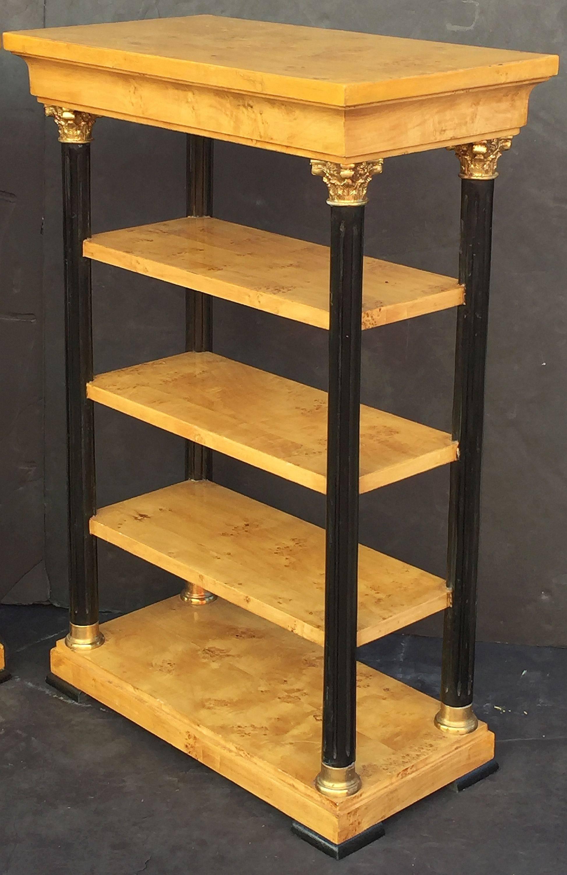 A fine pair of English open bookcases (or shelves) in the Biedermeier style, each shelving unit featuring a moulded top frieze of figured maple over four fluted column posts of ebonized wood, each post capped at top and bottom with gilt metal