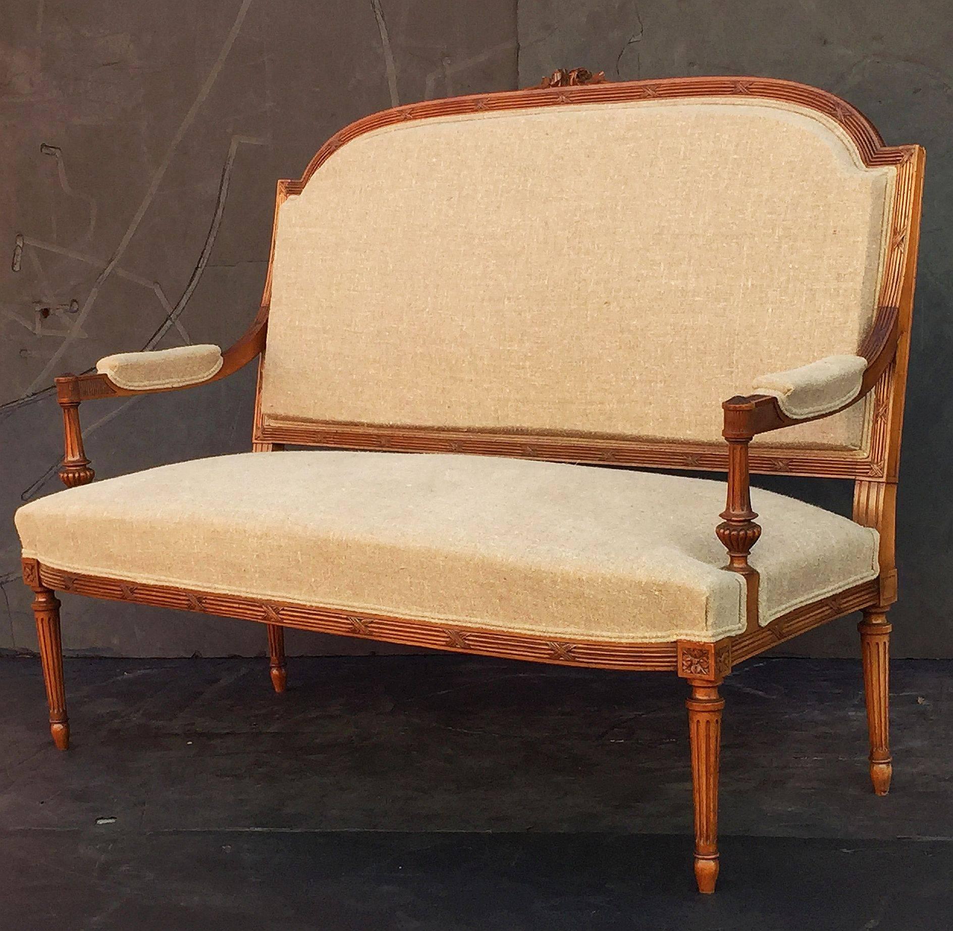 A handsome French settee featuring an upholstered back, arms, and seat on a frame of carved walnut, with foliate and ribbon accents, and  standing on fluted column legs.
