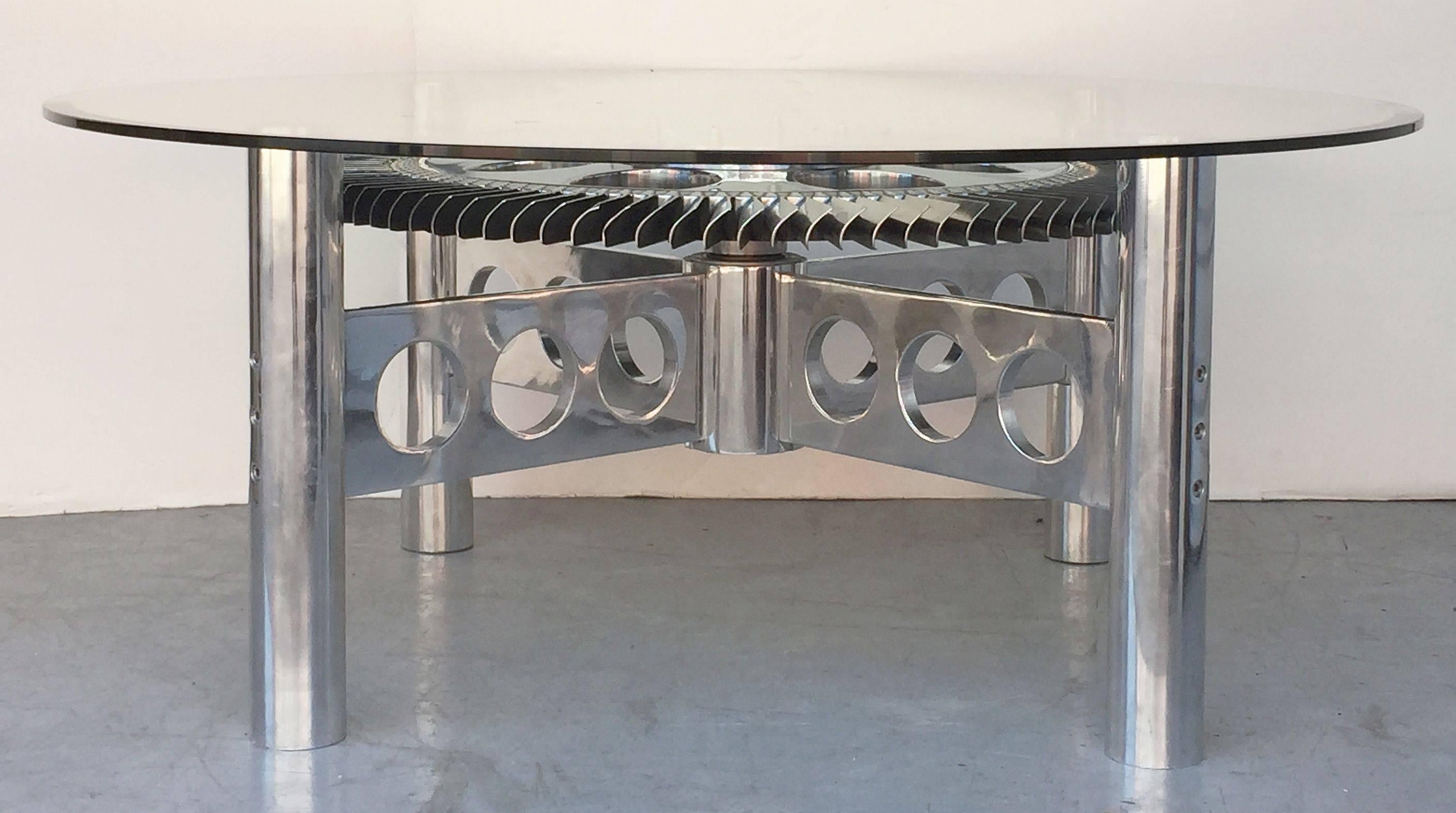 A stylish low cocktail or coffee table from England featuring a round glass top (48" diameter) with a beveled edge set upon base with an authentic Rolls Royce rotating impeller from a British military jet engine, mounted to a four-post frame of