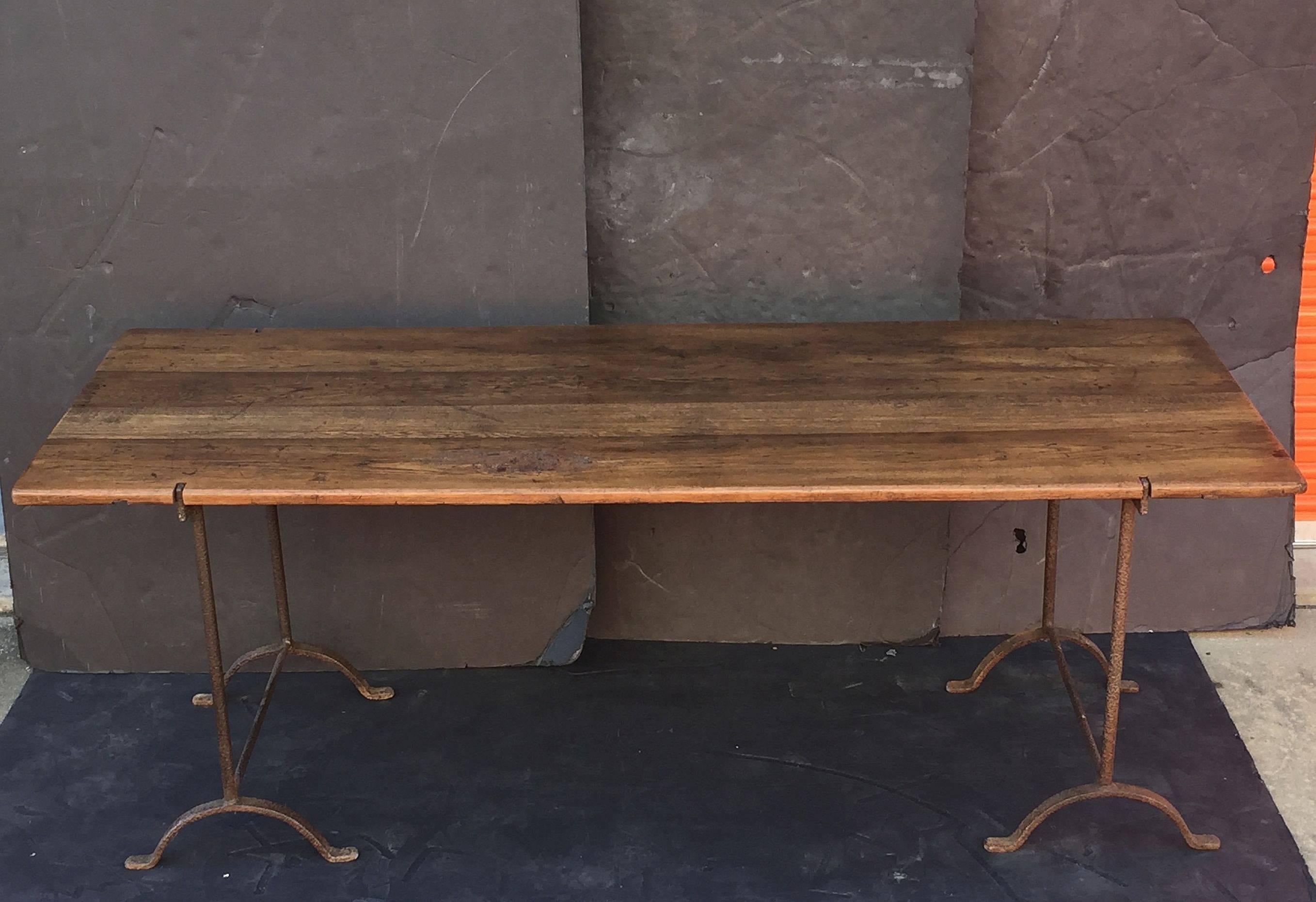 A large English trestle table featuring a novel design of a handsomely patinated plank wood top with notches on opposing ends for two wrought iron supports.

Dimensions are H 30 1/2