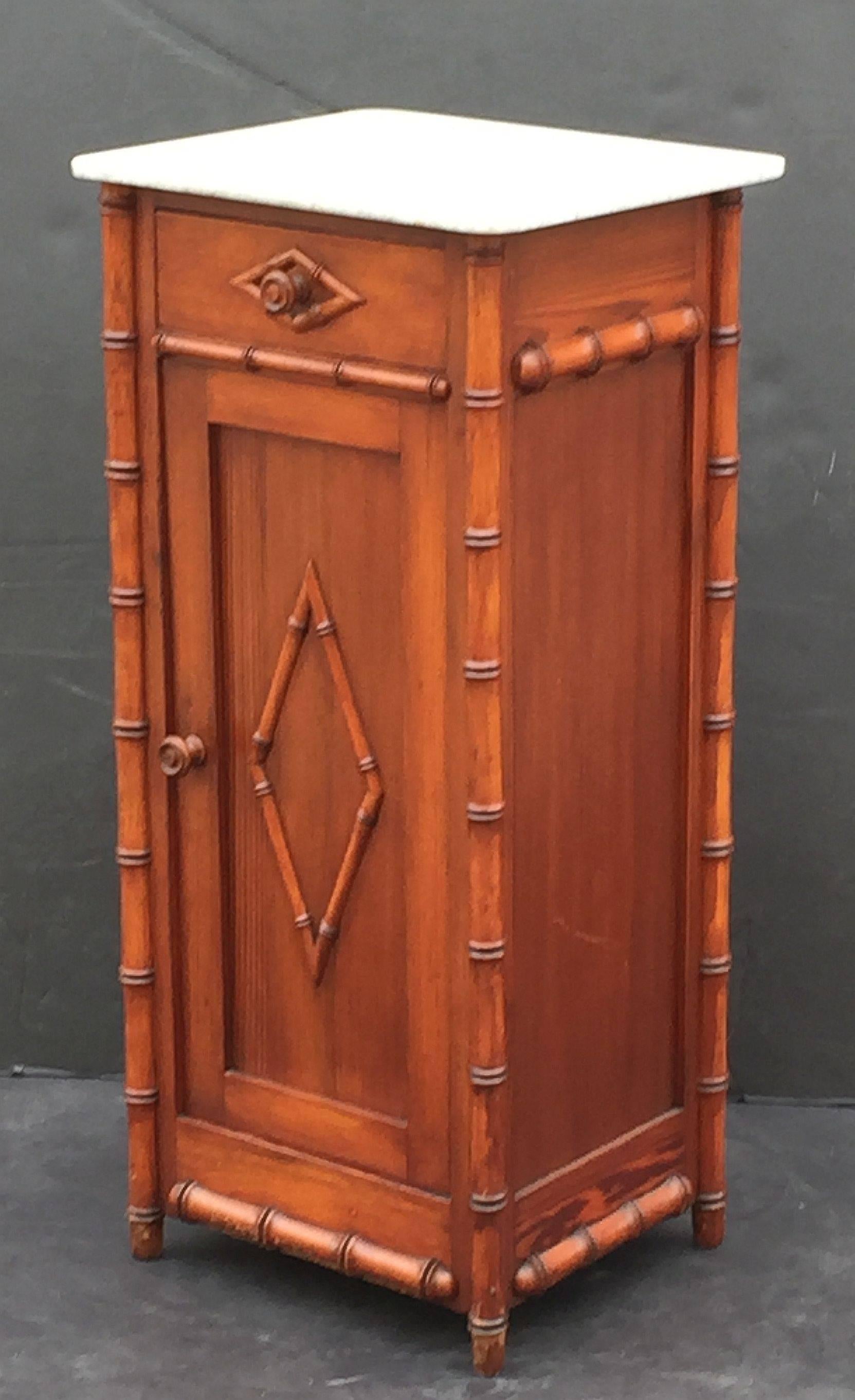 A handsome French faux bamboo nightstand (or commode) of long-leaf pine, featuring a white marble top with grey accents, over a frieze with drawer and cabinet door. The cabinet door opening to an interior with one shelf.
The whole accentuated by a