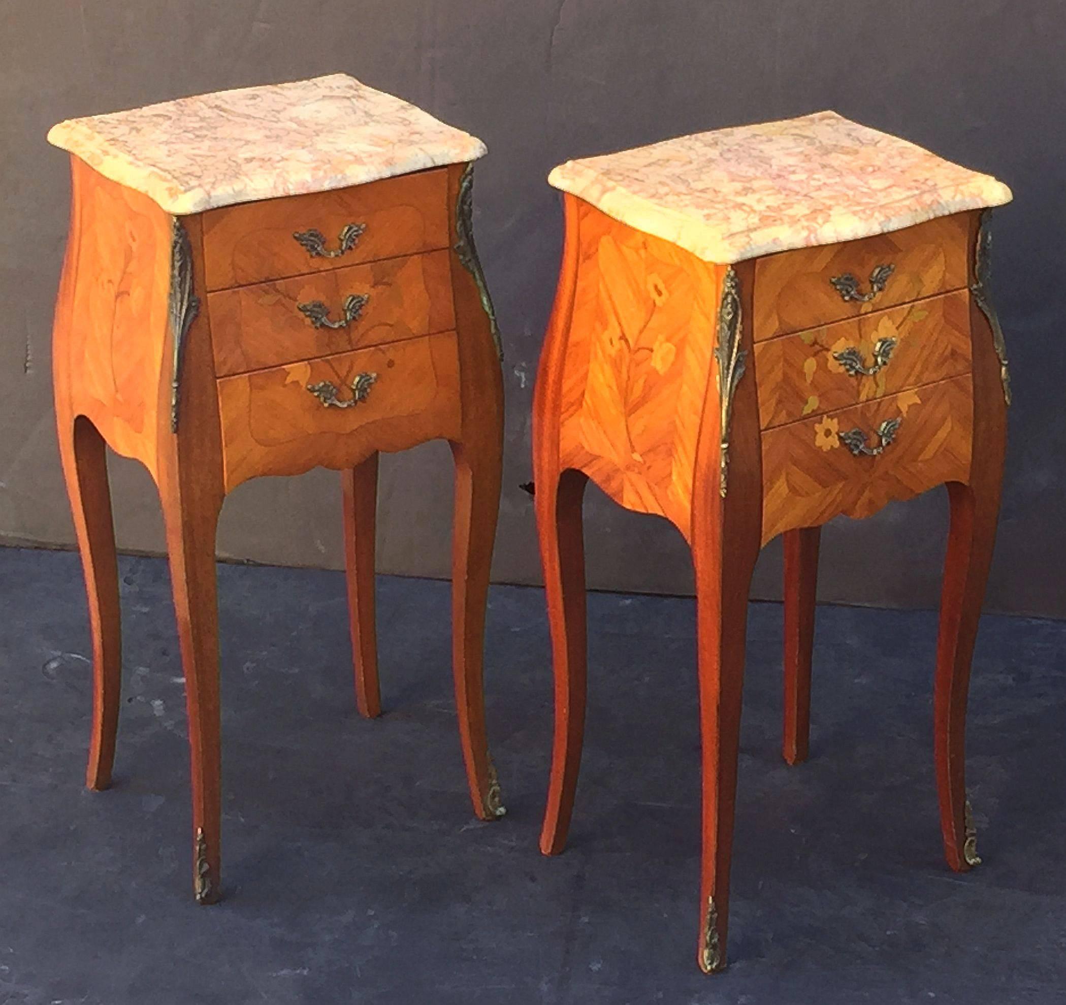 A fine pair of French bedside end tables or night stands, each stand featuring a figured marble-top with serpentine edge over a frieze with three inlaid drawers with decorative brass pulls, marquetry sides, ormolu accents, and apron bottoms.
Both