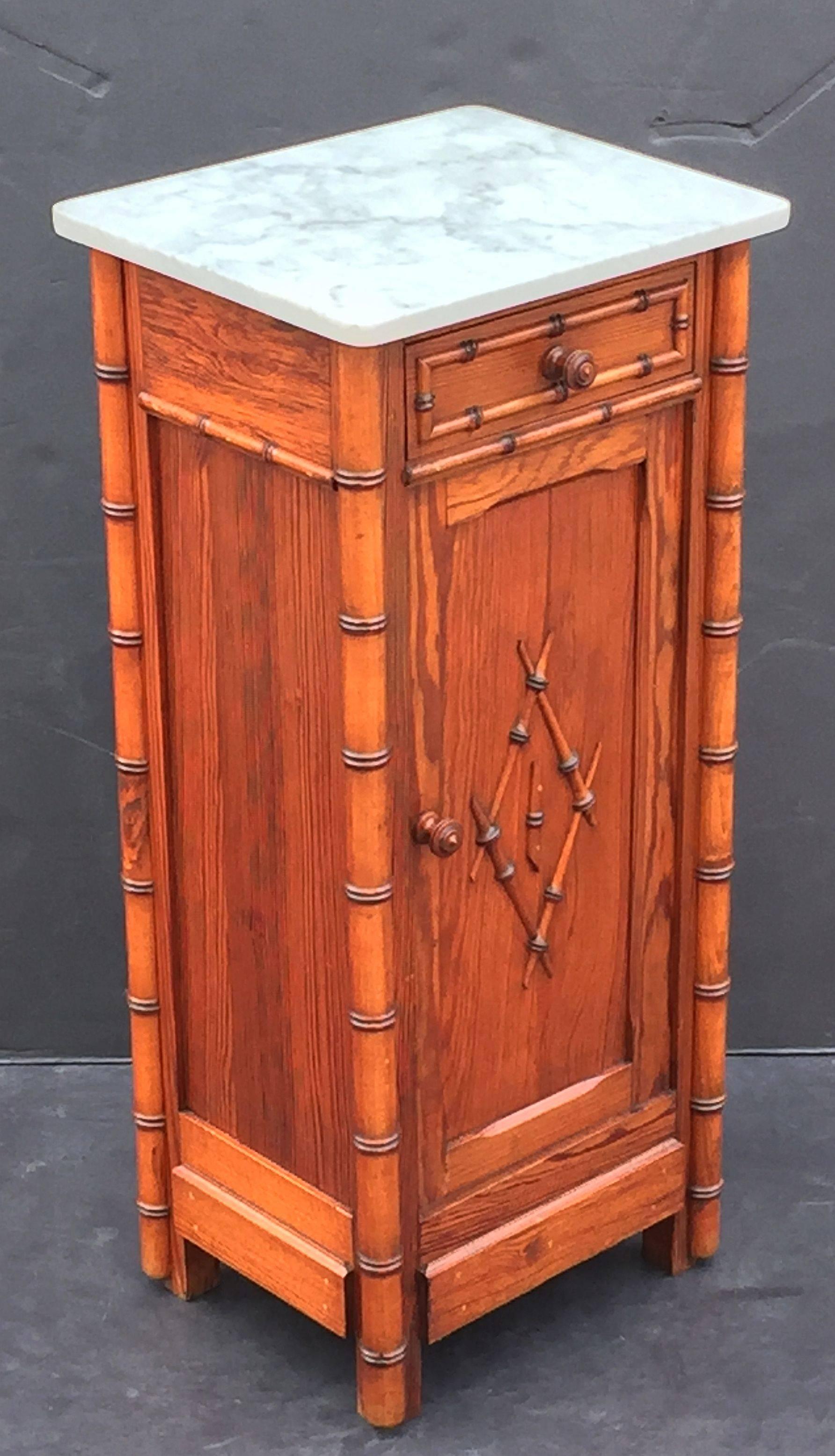 A handsome French faux bamboo nightstand (or commode) of long-leaf pine, featuring a white marble top with grey accents, over a frieze with drawer and cabinet door. The cabinet door opening to an interior with one shelf.
The whole accentuated by a